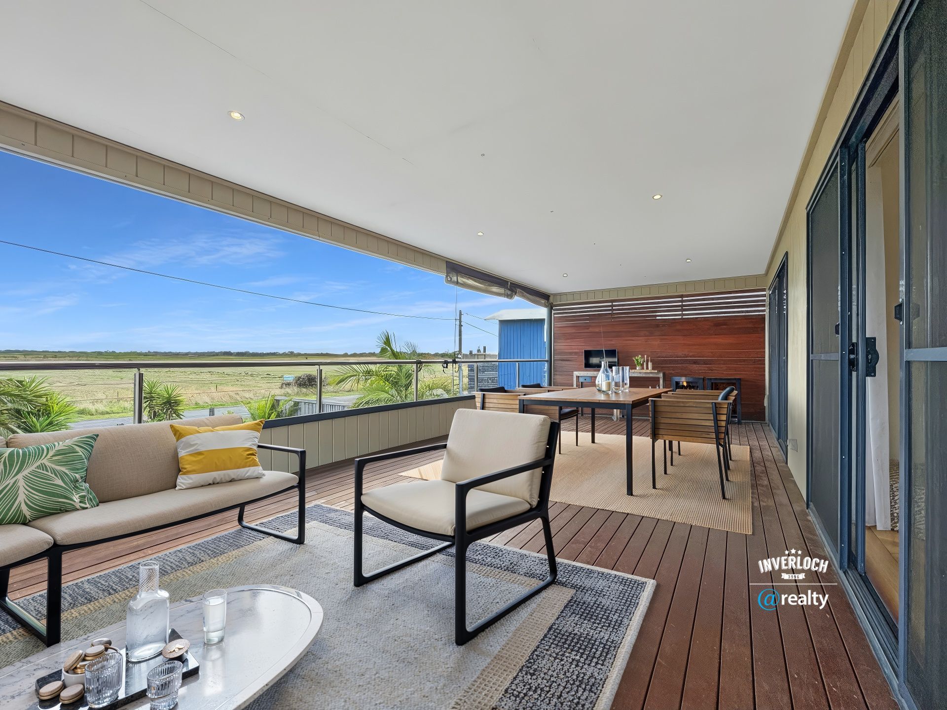 Outdoor deck with seating, dining area, and scenic view of a field under a blue sky.