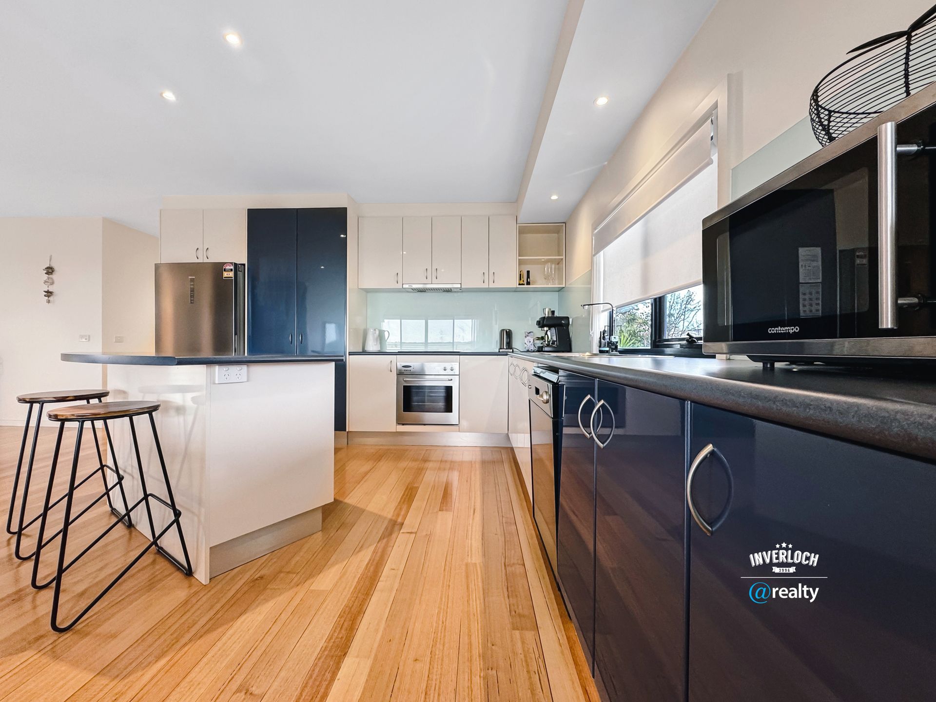 A kitchen with wooden floors , blue cabinets , stainless steel appliances and a microwave.