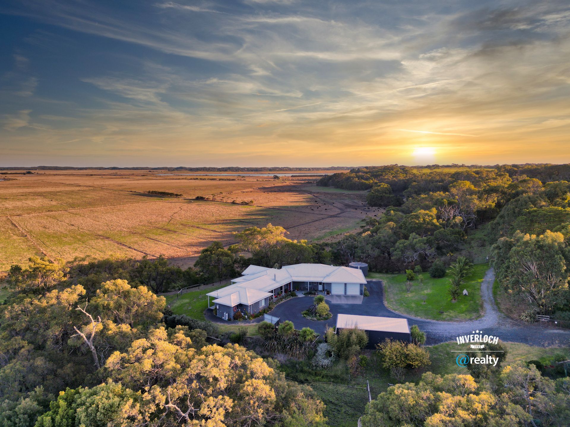 An aerial view of a house in the middle of a field at sunset.