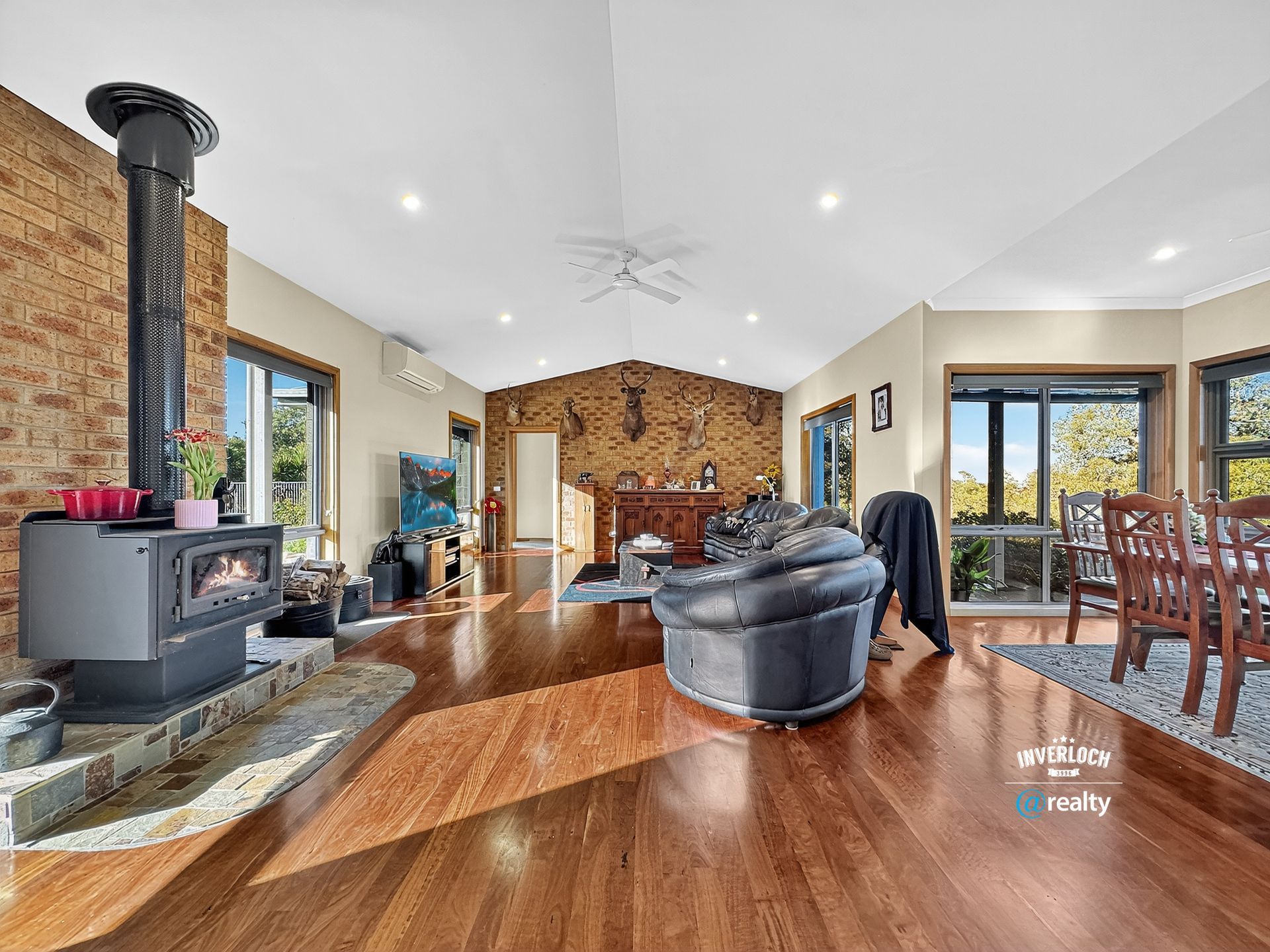 Living room with wood-burning fireplace, wooden floor, windows, and leather sofa.