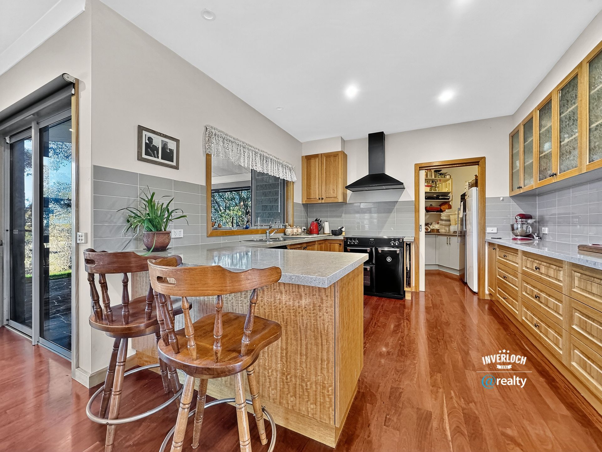 Kitchen with island, wooden cabinets, and bar stools. Dark floors, light gray walls, and a view of the outdoors.