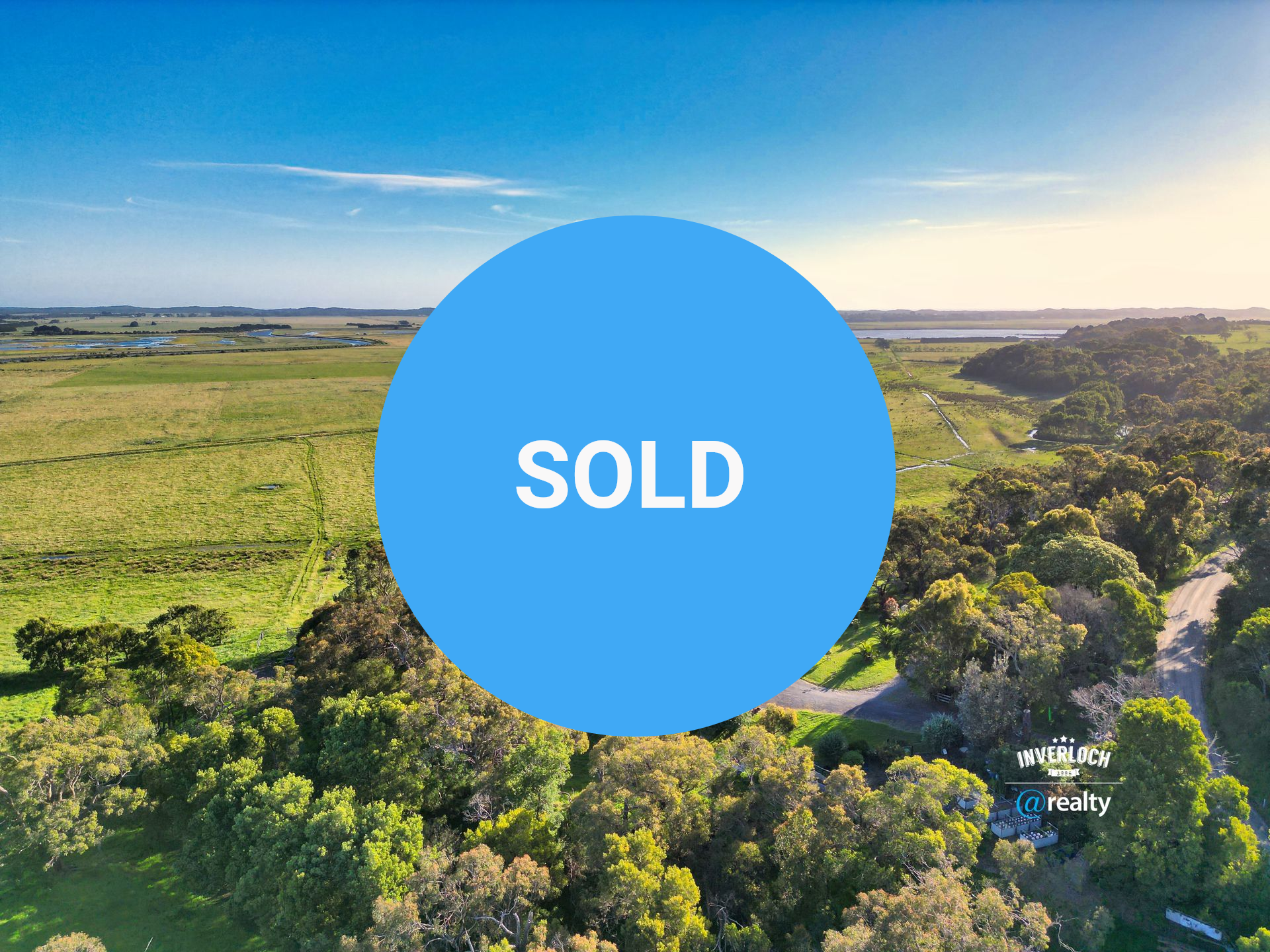 House with driveway surrounded by trees, overlooking a field at sunset.
