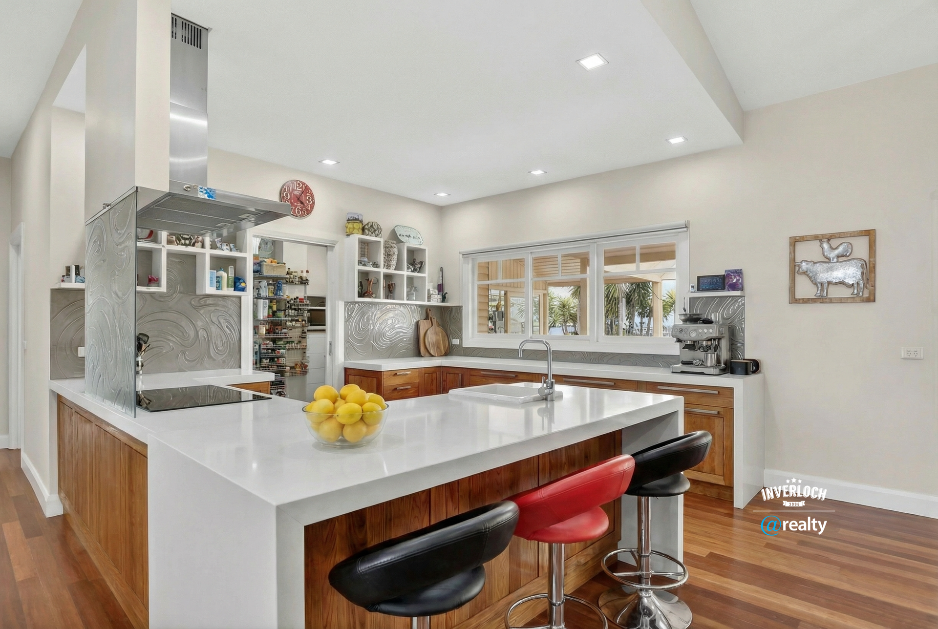 Kitchen with white countertop island, wooden cabinets, and three bar stools.