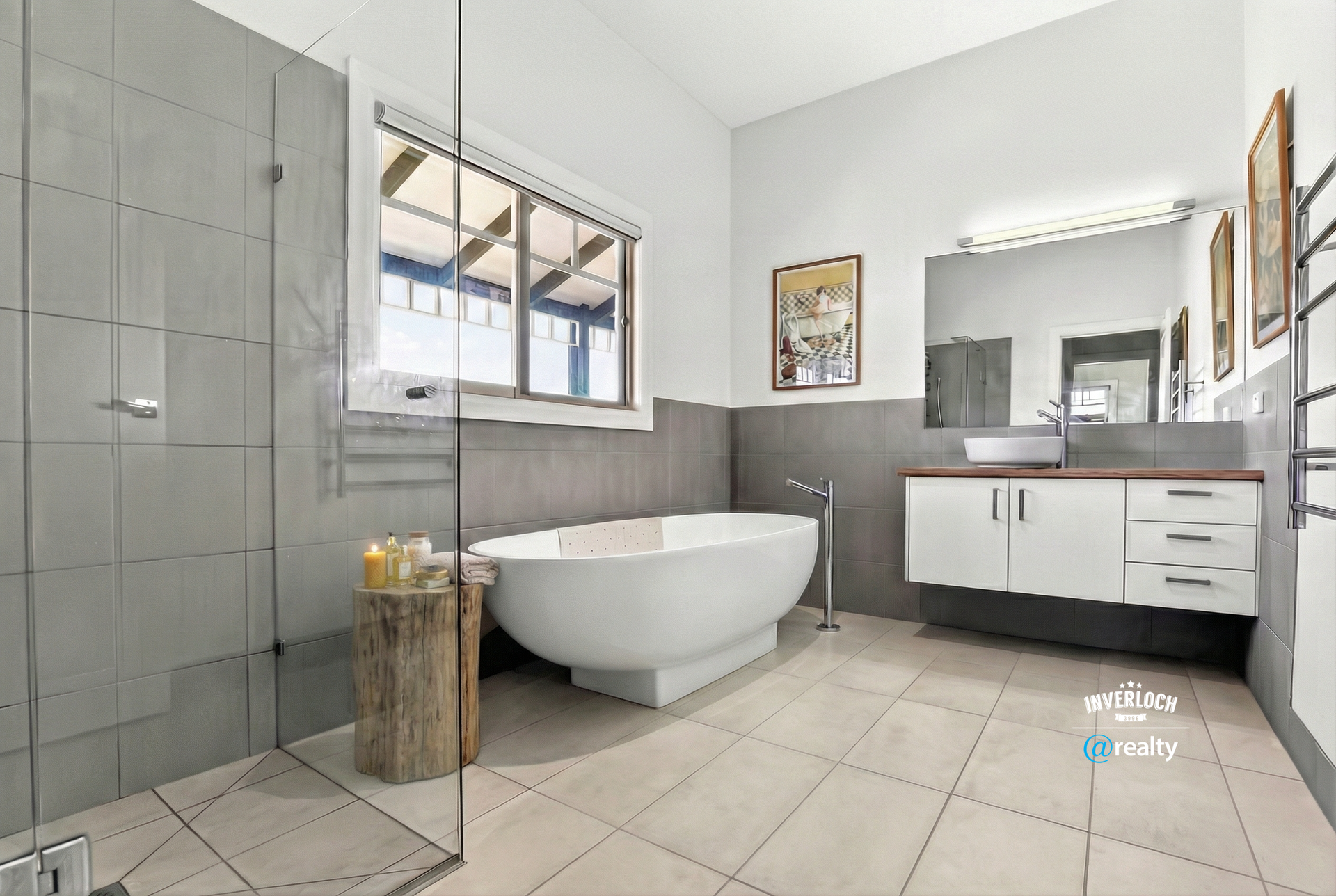 Bathroom with a freestanding white tub, grey tile walls, white vanity, and large window.