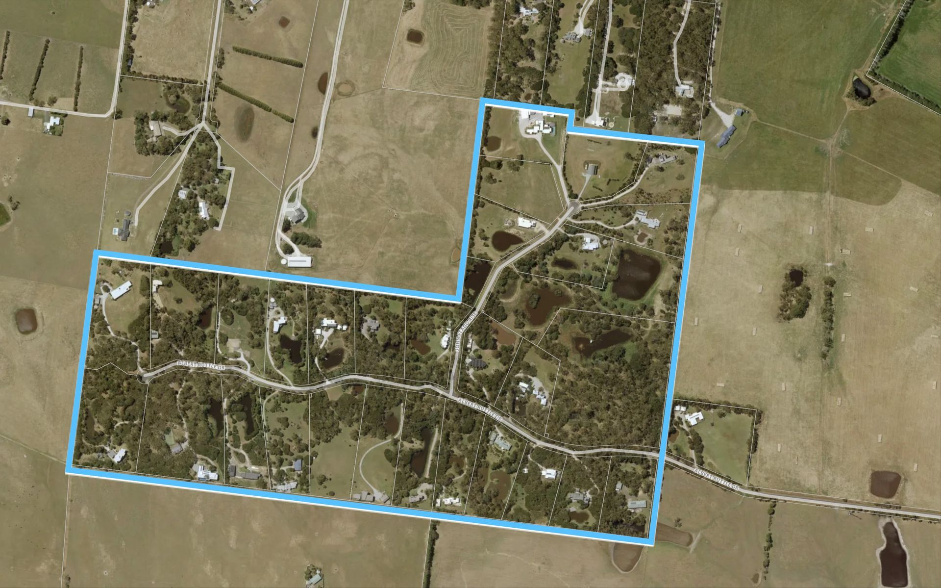Aerial view of a rural property outlined in blue. Contains houses, trees, roads, and open fields.