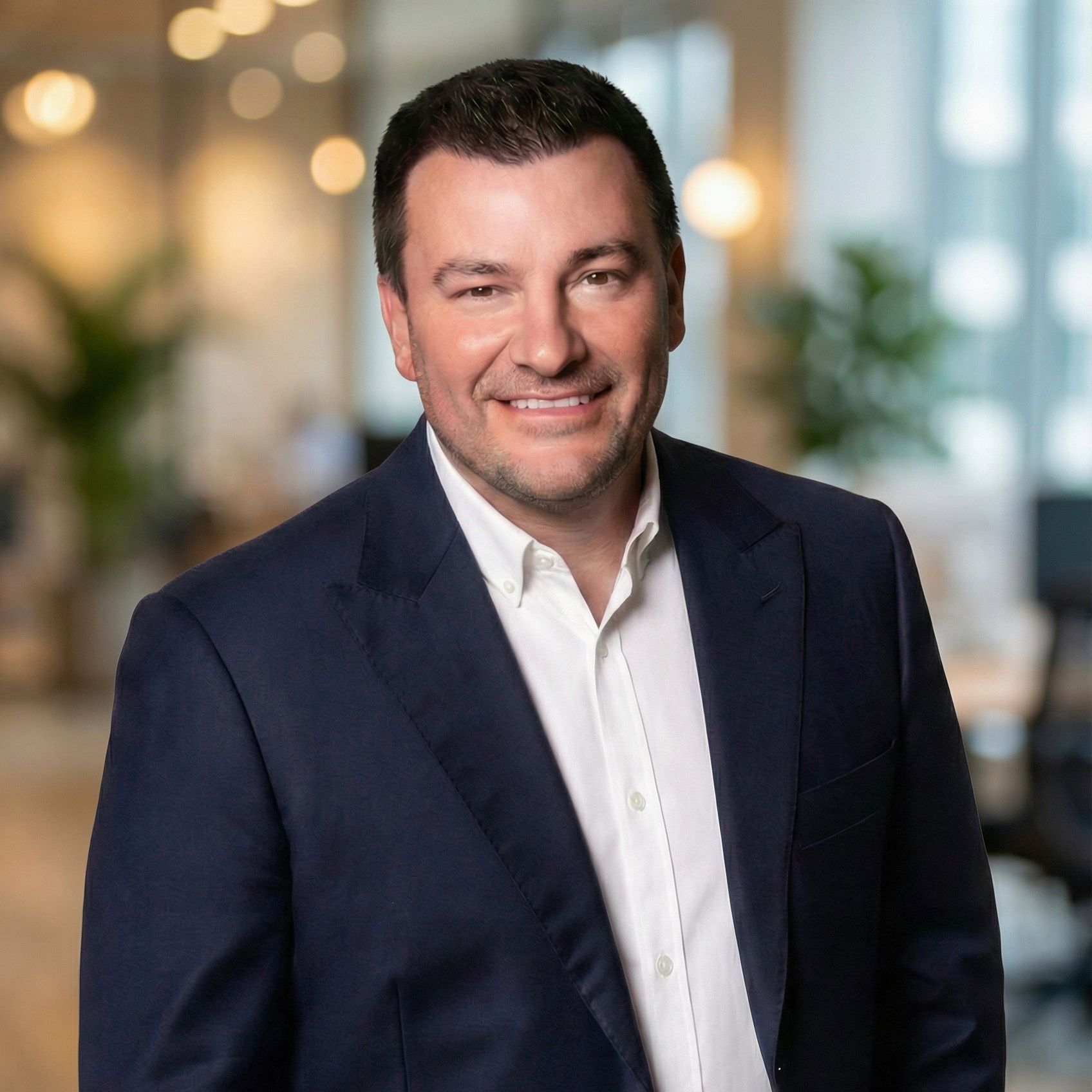 Man in a blue blazer and white shirt, smiling in an office setting.