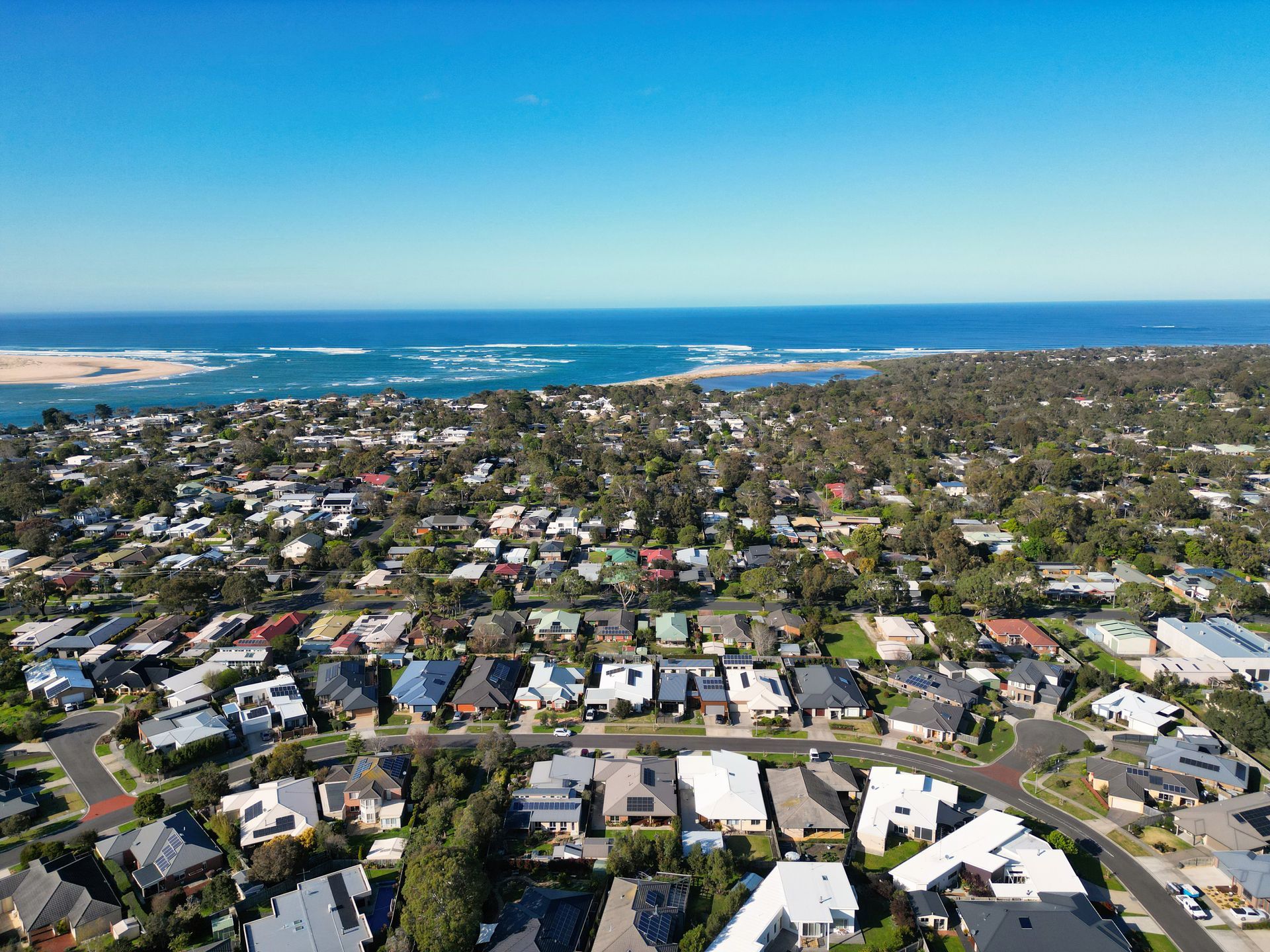 Aerial view of a coastal town with a beach, road, and houses nestled among trees.