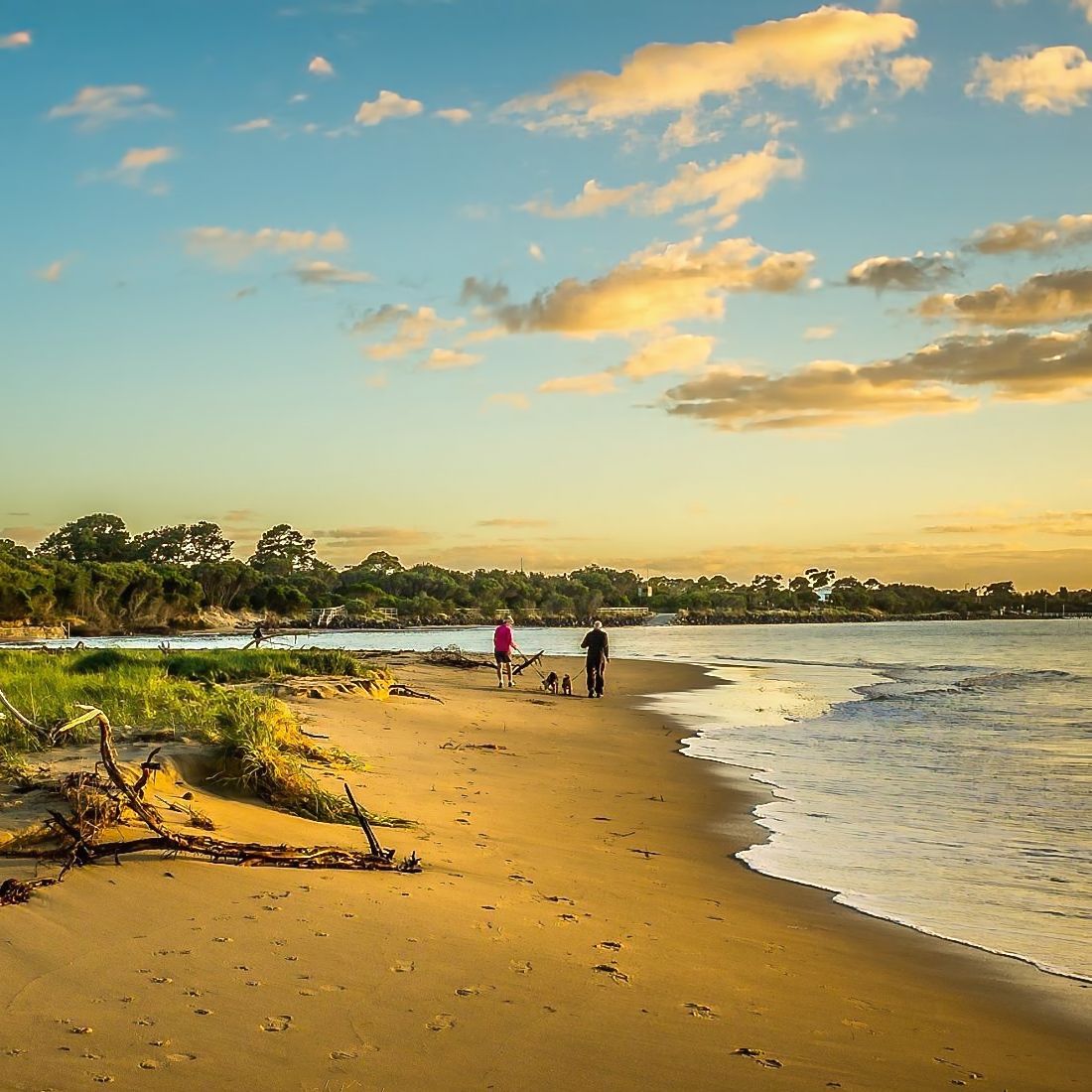 Sunset beach with two people walking along the shoreline under a partly cloudy sky