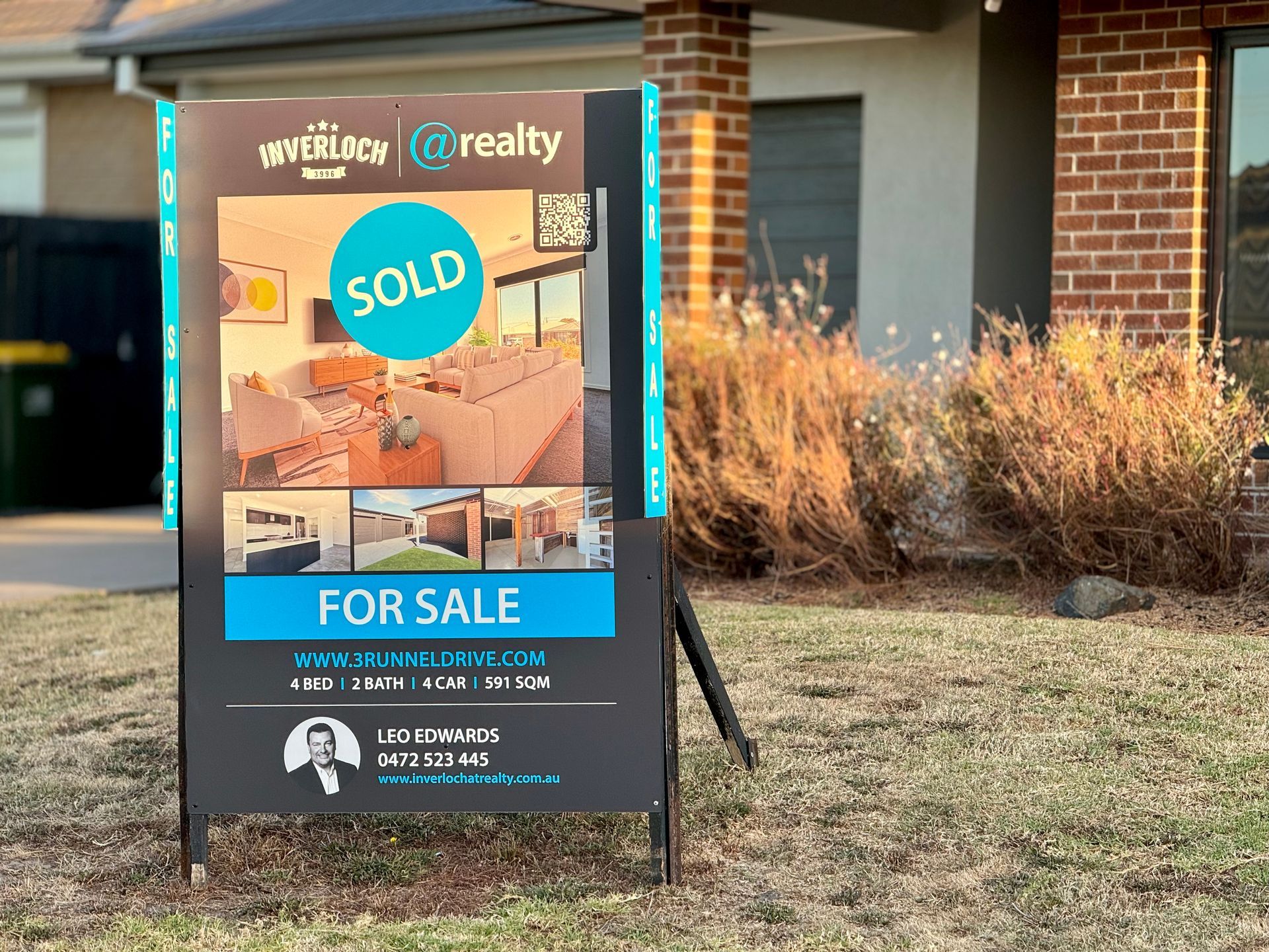 A for sale sign is sitting in front of a brick house