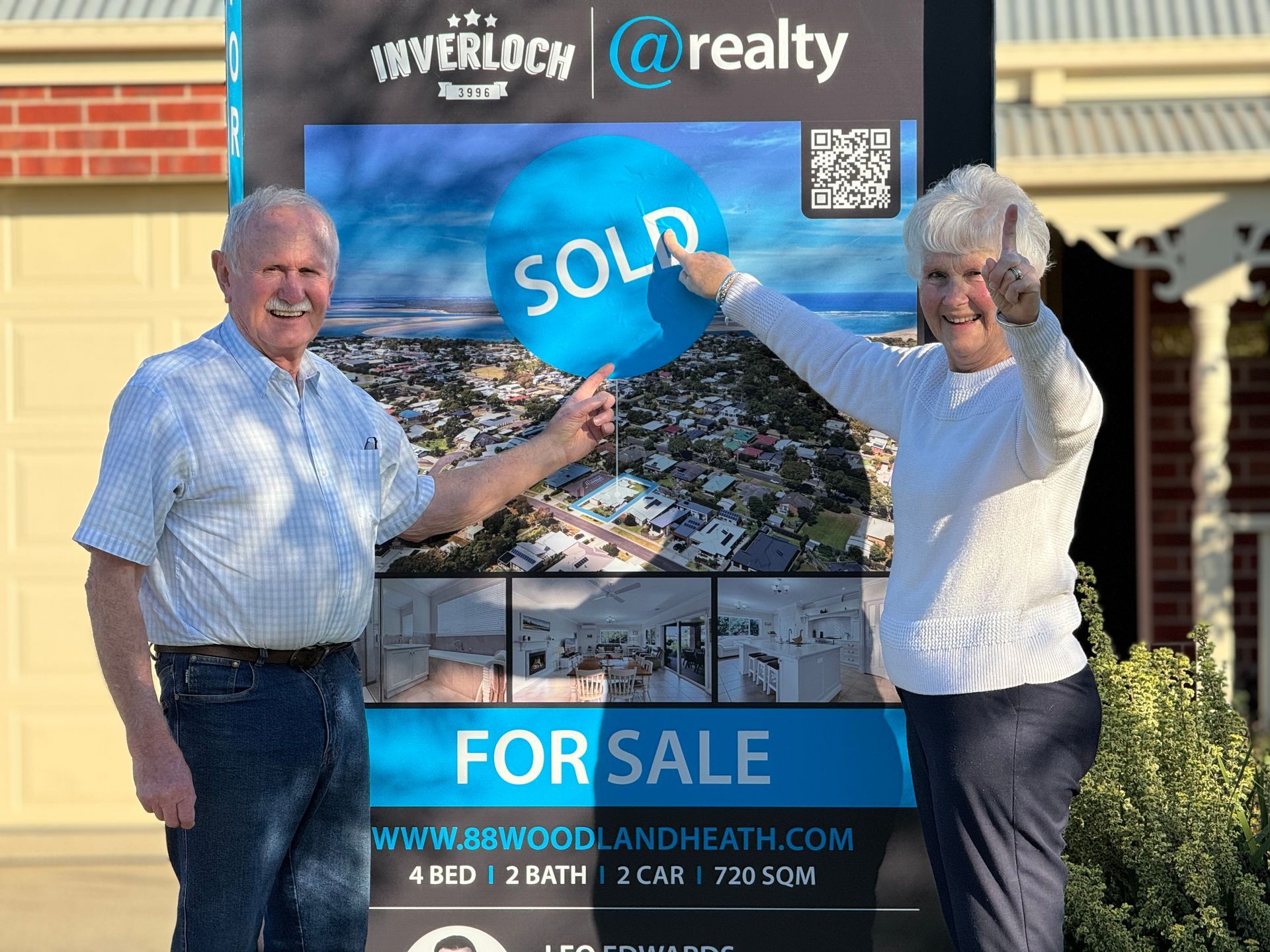 A man and woman are holding a sold sign in front of a for sale sign.