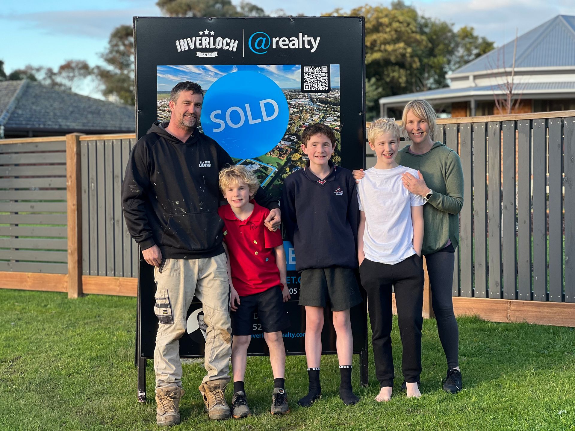 A family is posing for a picture in front of a sold sign.