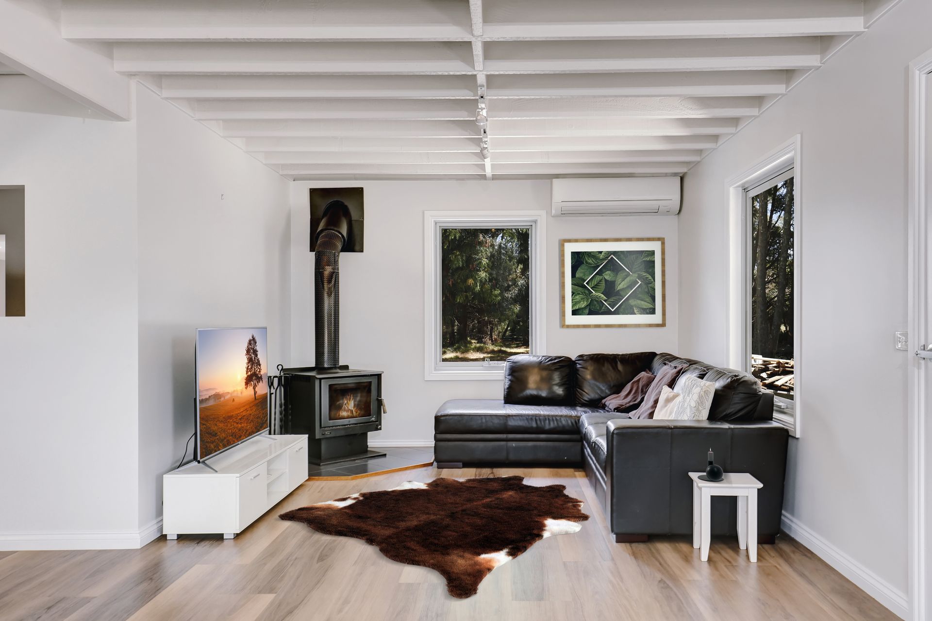 Cozy living room with fireplace, leather sectional, rug, and windows overlooking trees.