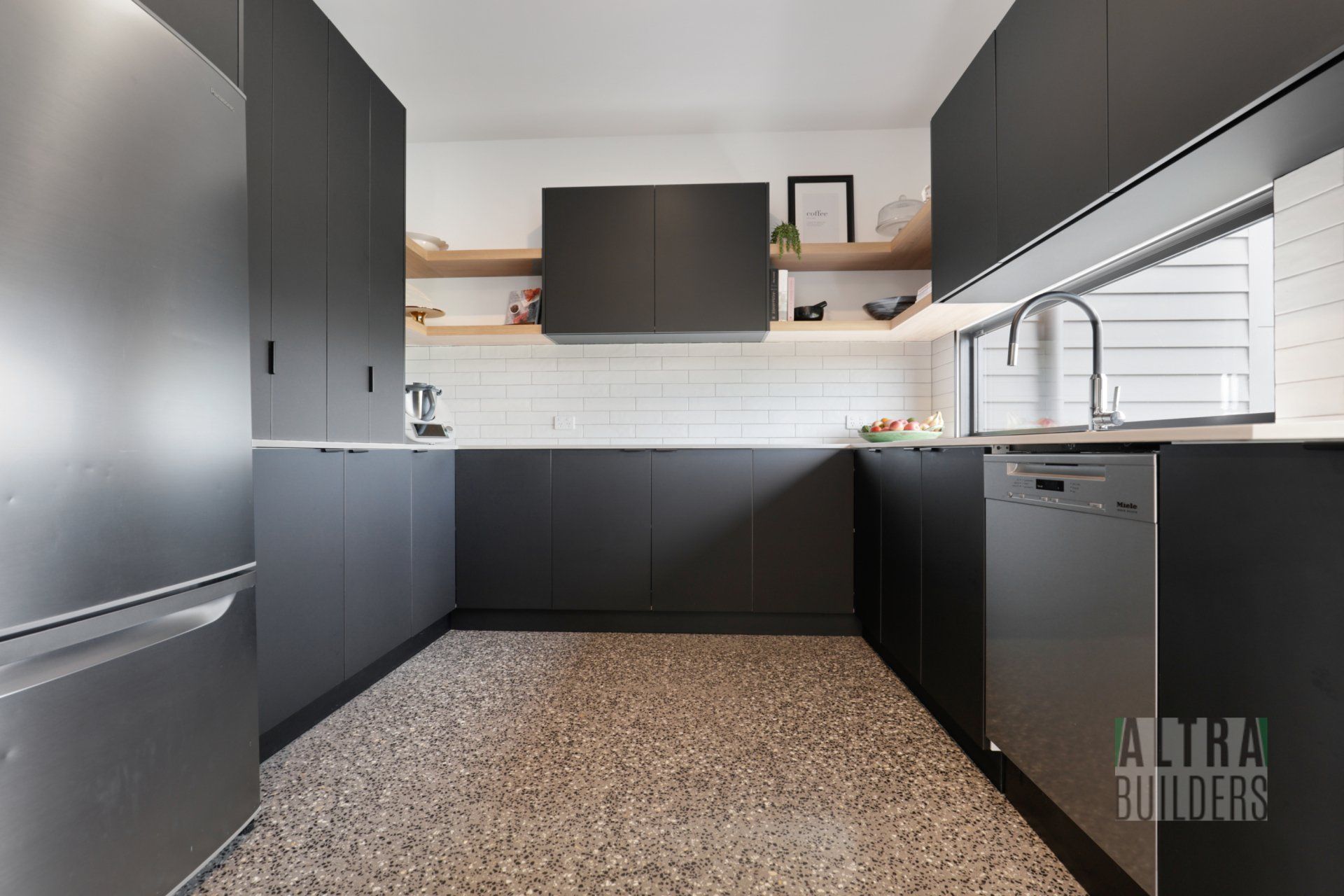 A kitchen with black cabinets and a stainless steel refrigerator.