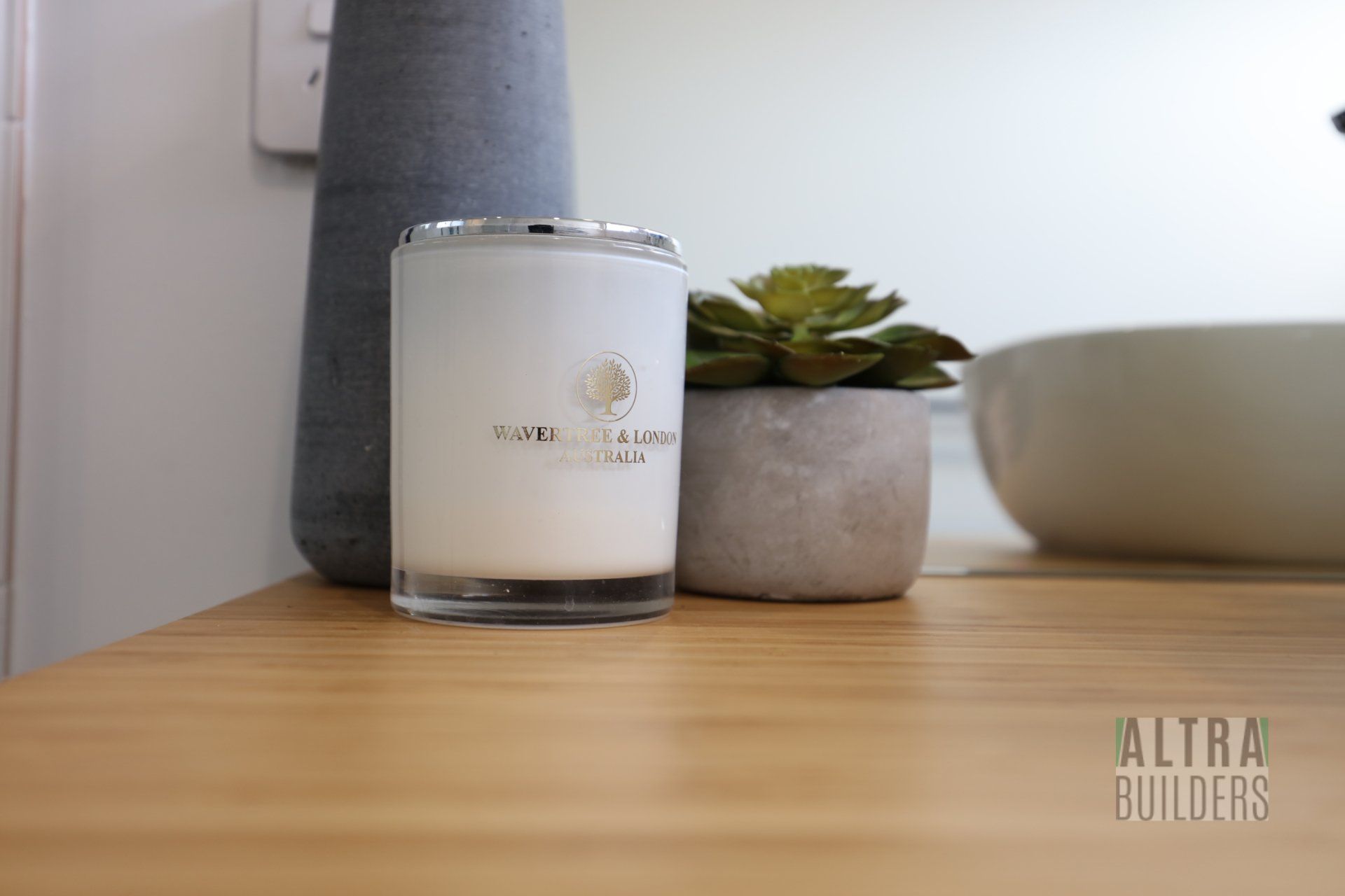 A white candle is sitting on a wooden table next to a potted plant.