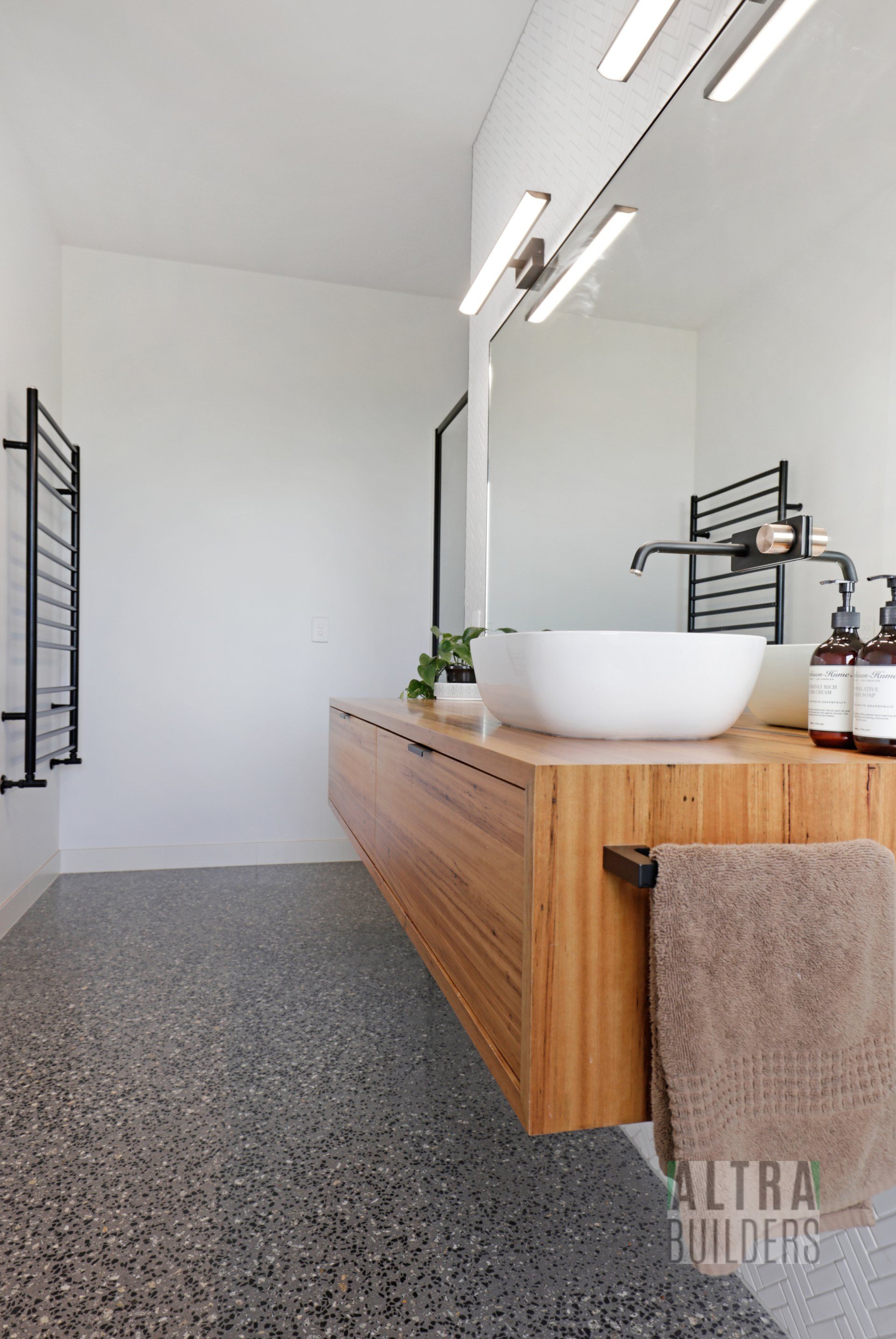 A bathroom with a wooden vanity , sink , mirror and towel rack.