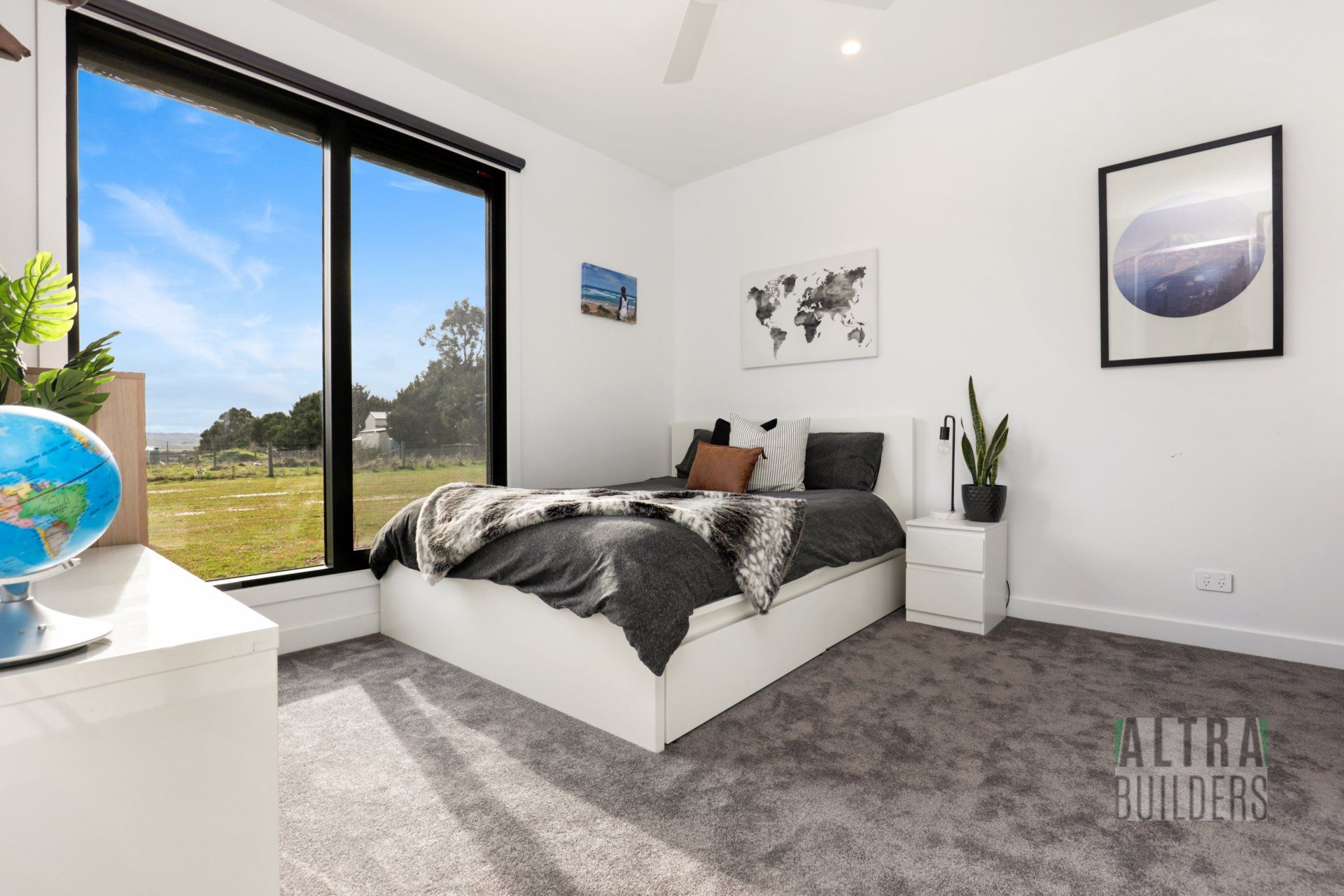 A bedroom with a bed , nightstand , globe and a large window.