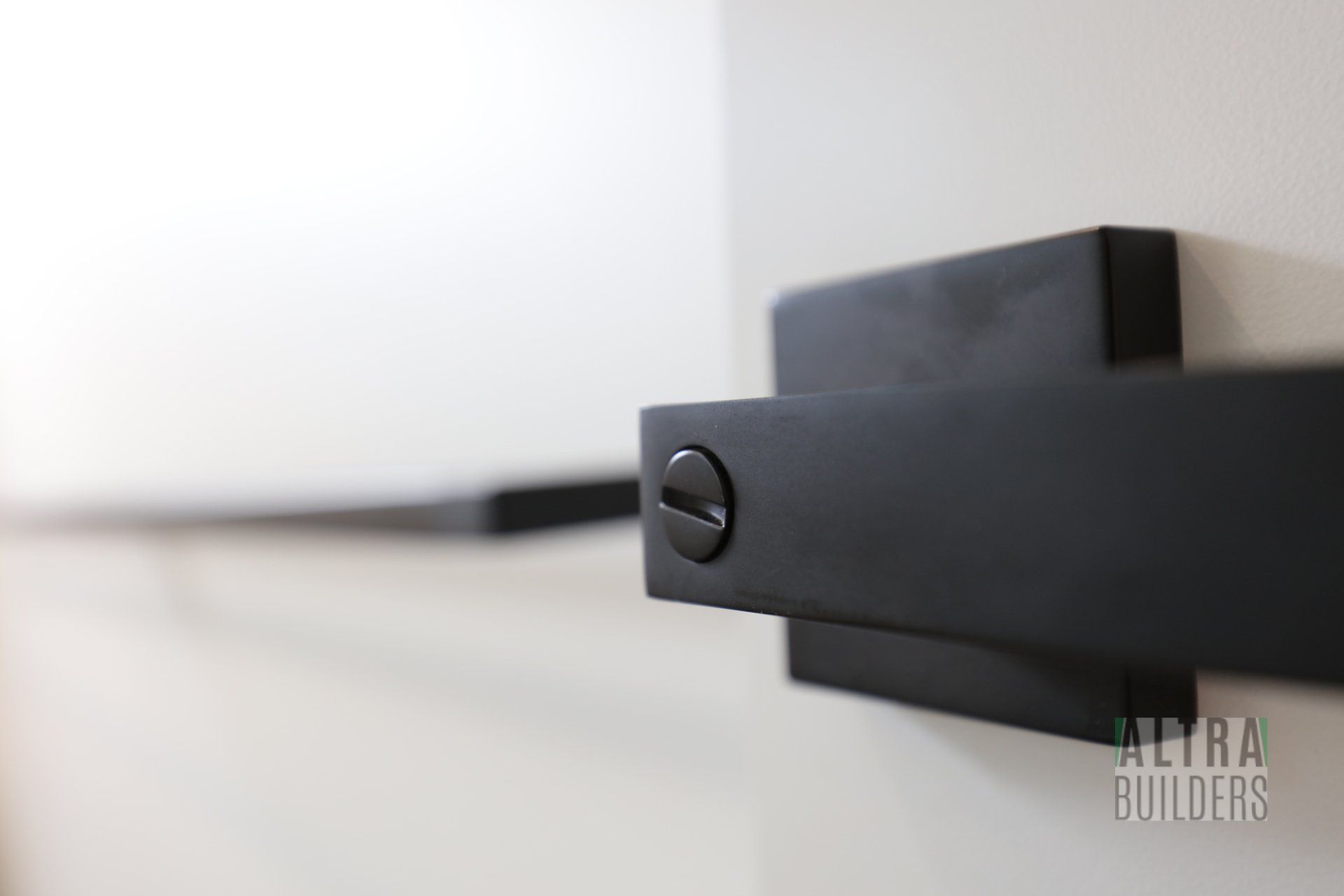A close up of a black door handle on a white wall.
