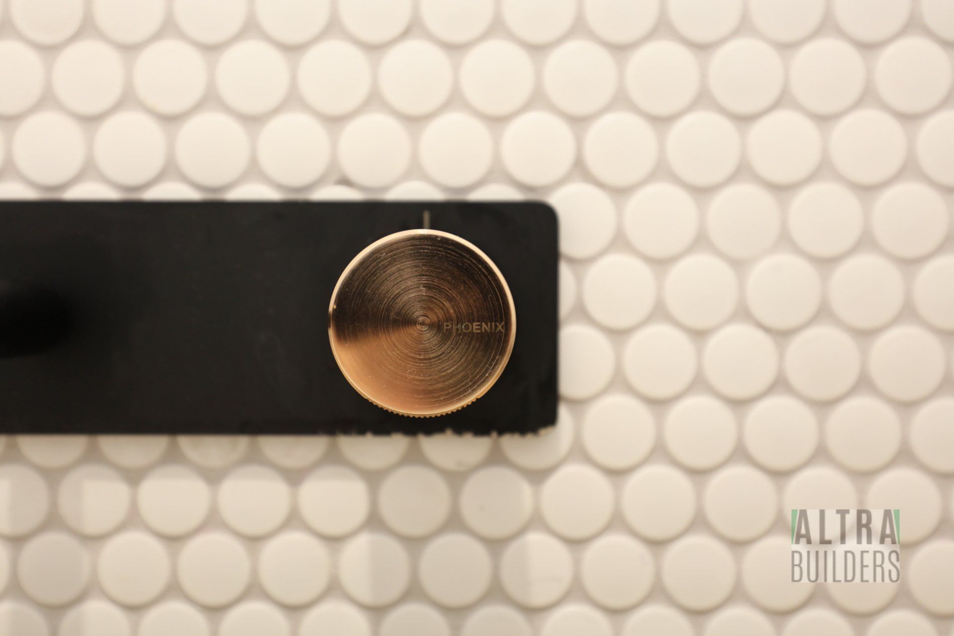A black and gold knob on a white tile wall
