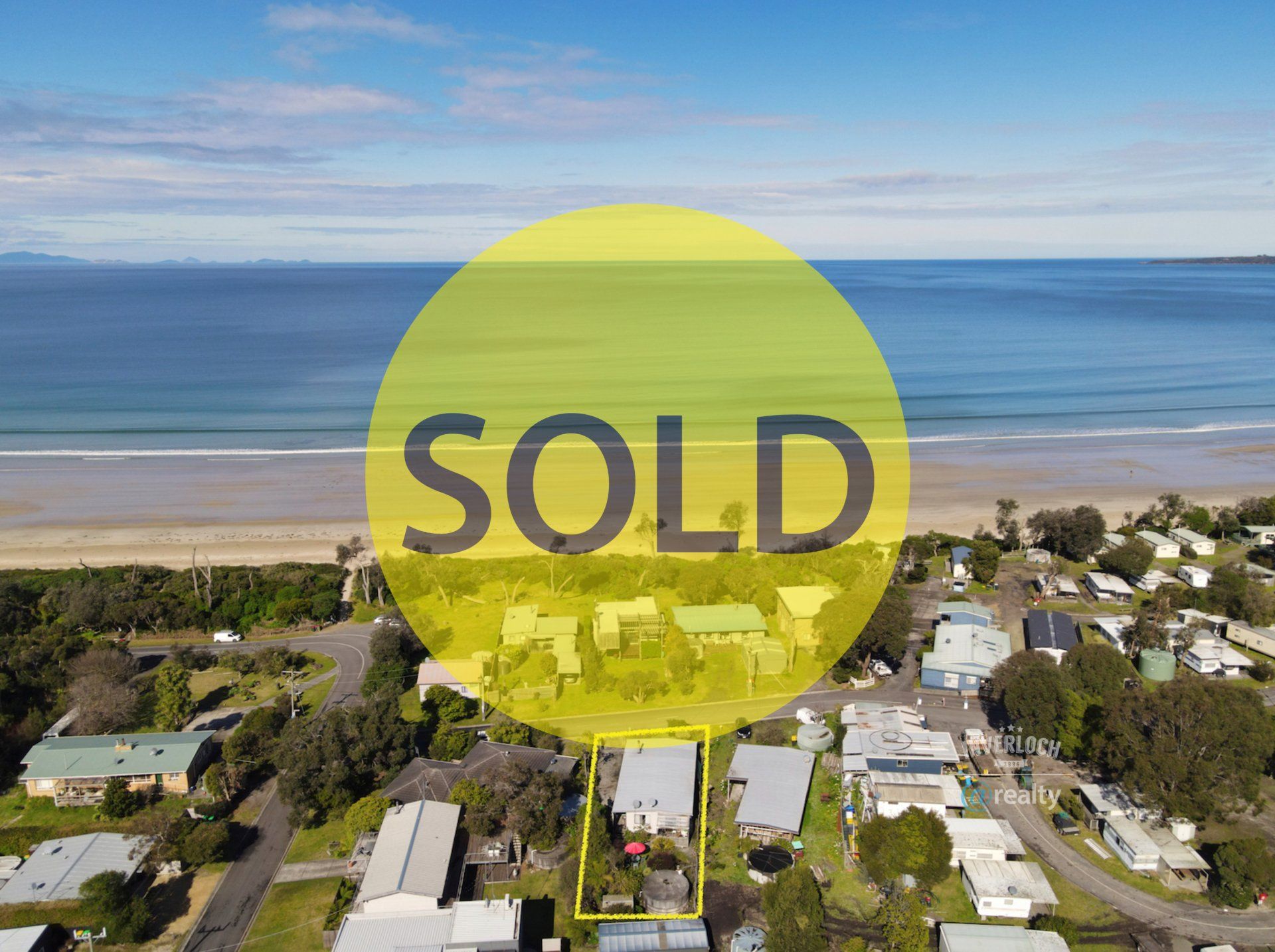 An aerial view of a beach with a sold sign in the foreground.