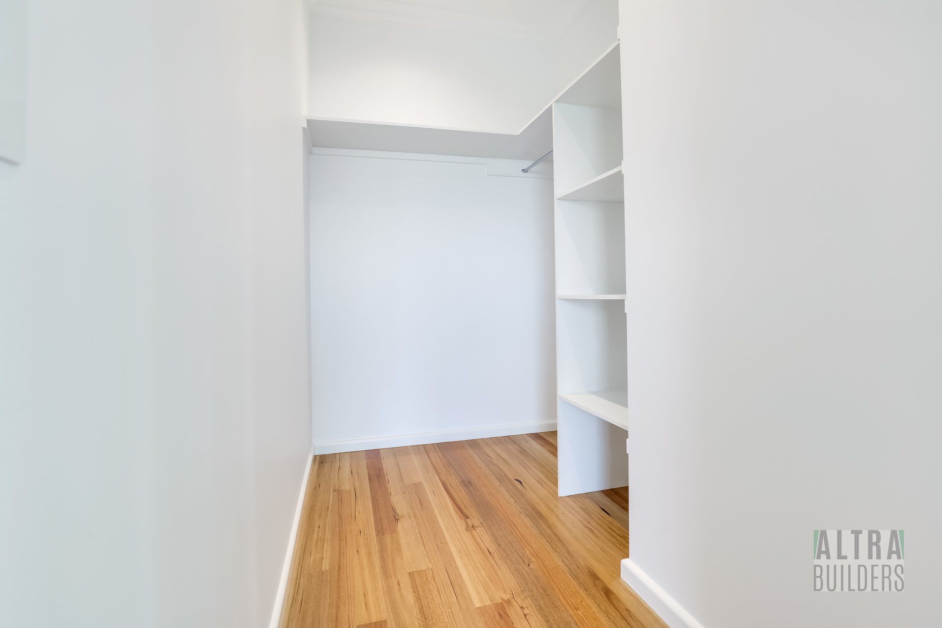 An empty walk in closet with hardwood floors and white walls.