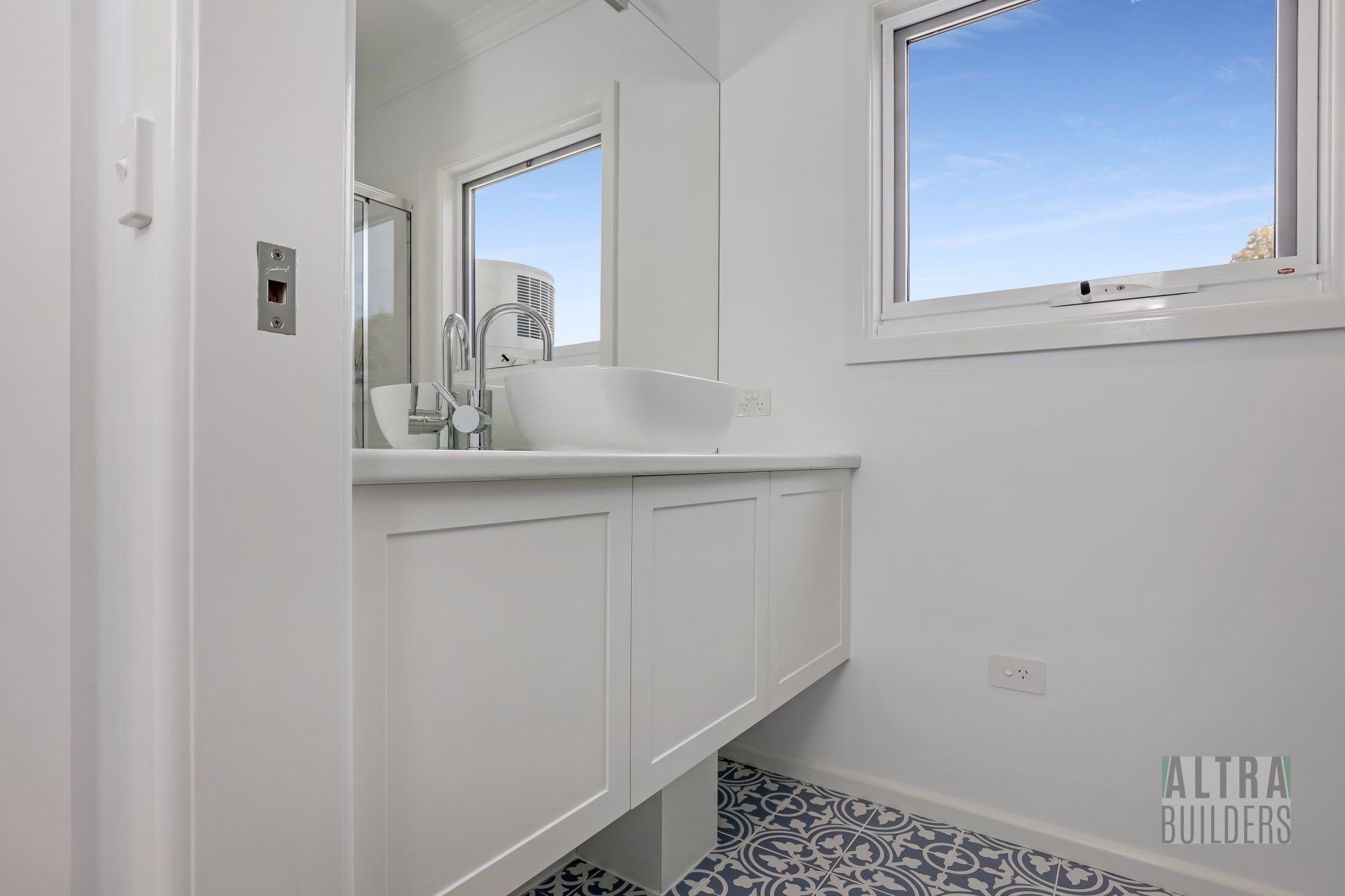 A bathroom with a sink , mirror and window.