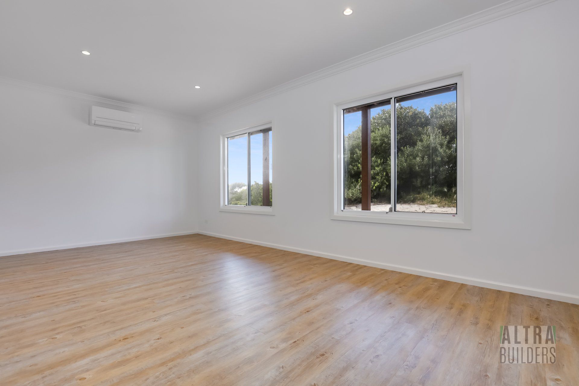 An empty living room with hardwood floors and two windows.