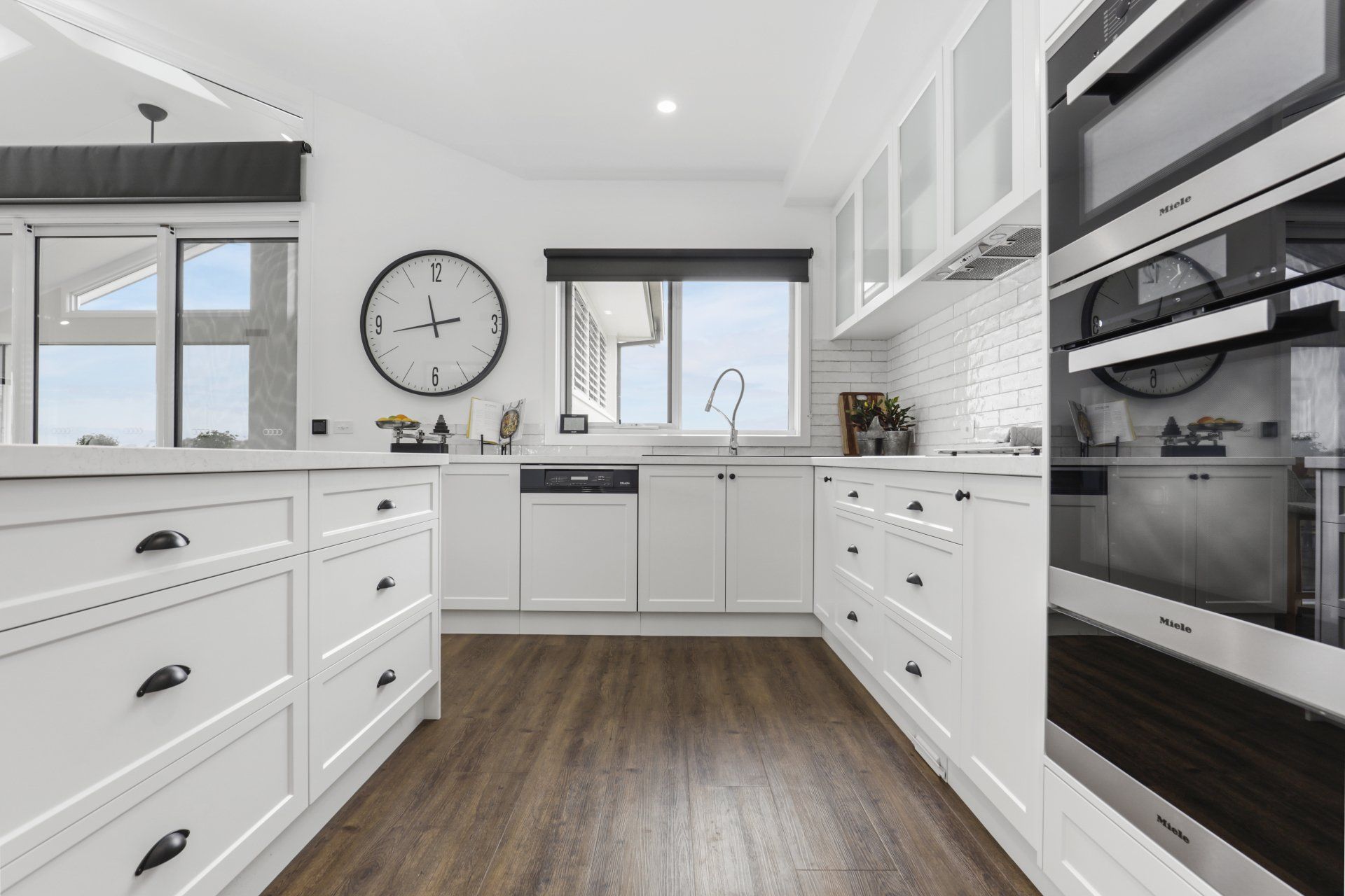 A kitchen with white cabinets and stainless steel appliances and a clock on the wall.