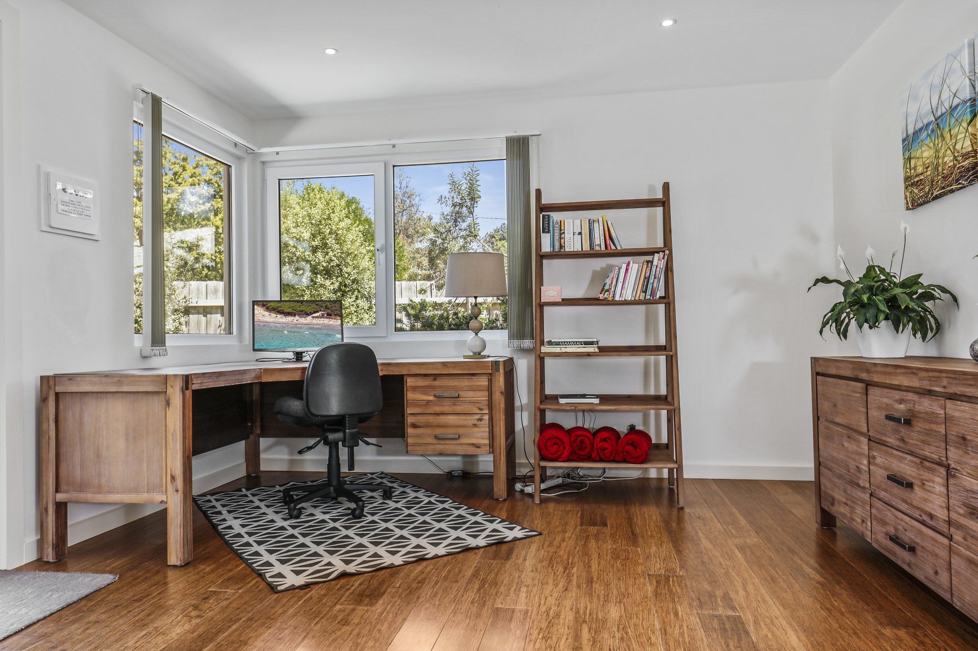 A room with hardwood floors , a desk , chair , dresser and bookshelf.