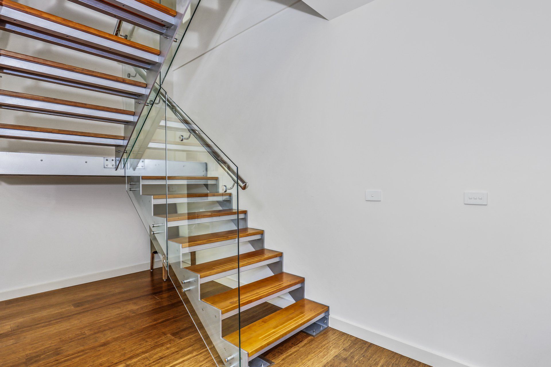 A modern staircase with wooden steps and a glass railing.