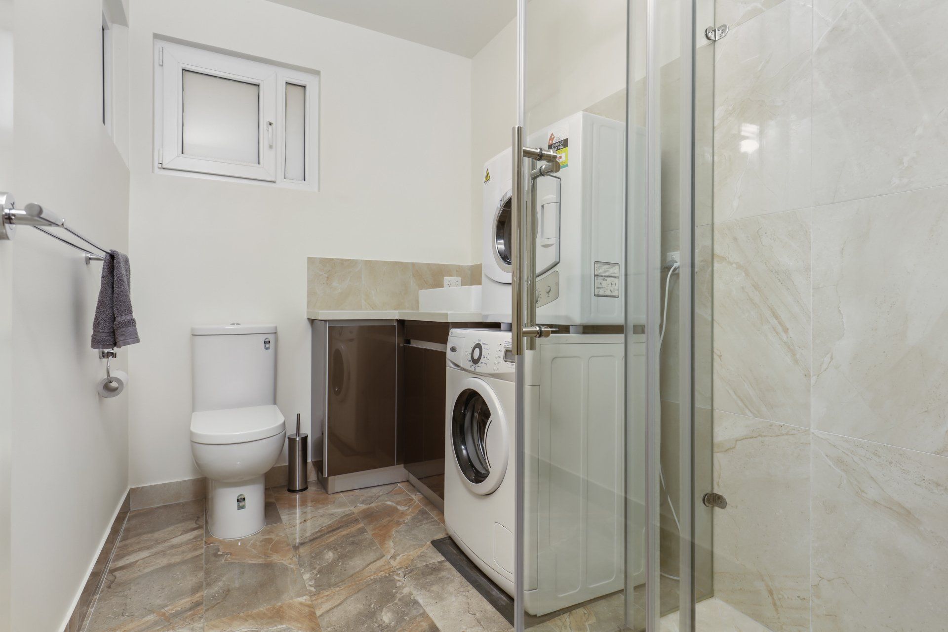 A bathroom with a toilet , washer and dryer , and shower.