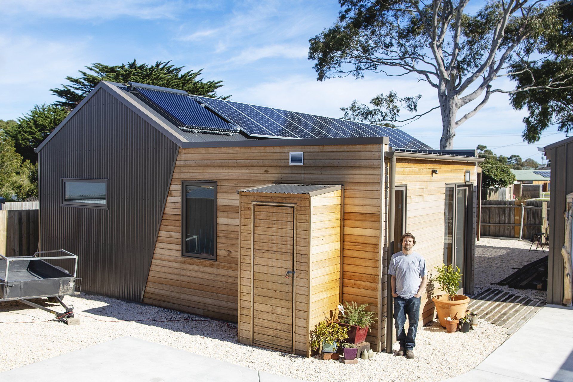 A man standing in front of a wooden house with solar panels on the roof