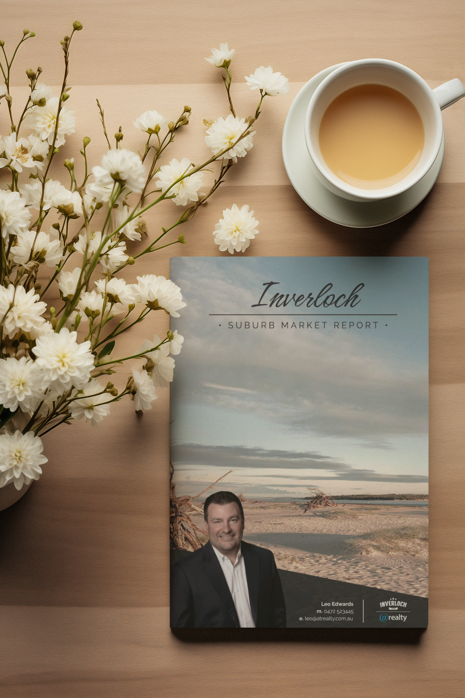 Book and cup of tea on a wooden table, with white flowers. The book cover features a man.