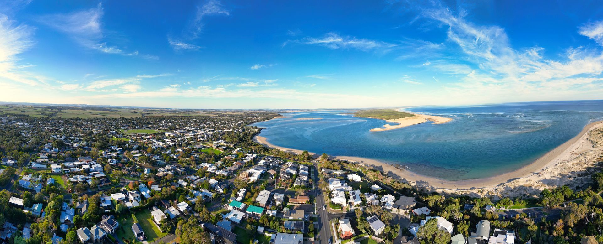 Aerial view of a coastal town, blue ocean, sandy beach, and clear sky.
