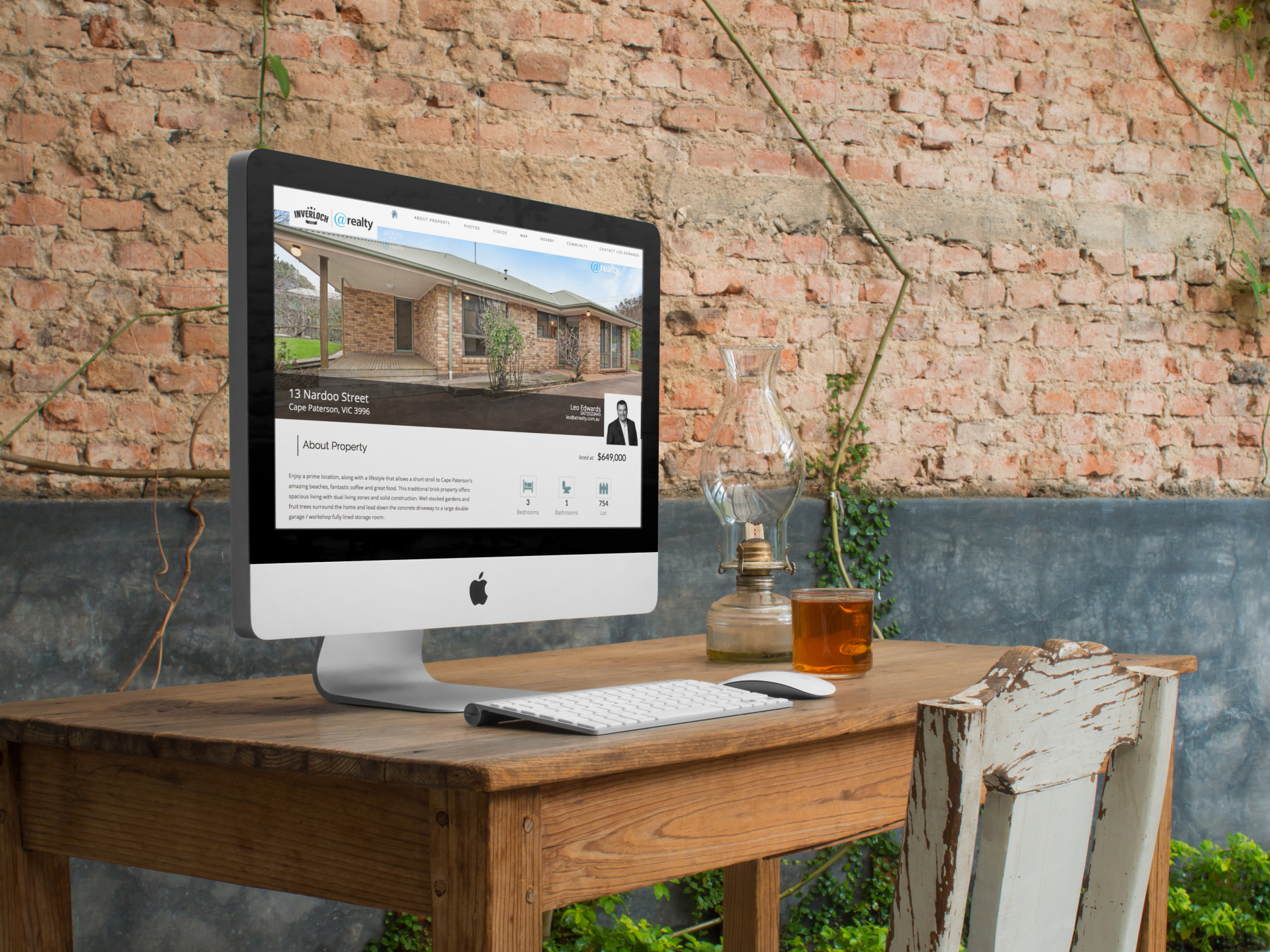 A computer is sitting on a wooden desk in front of a brick wall.