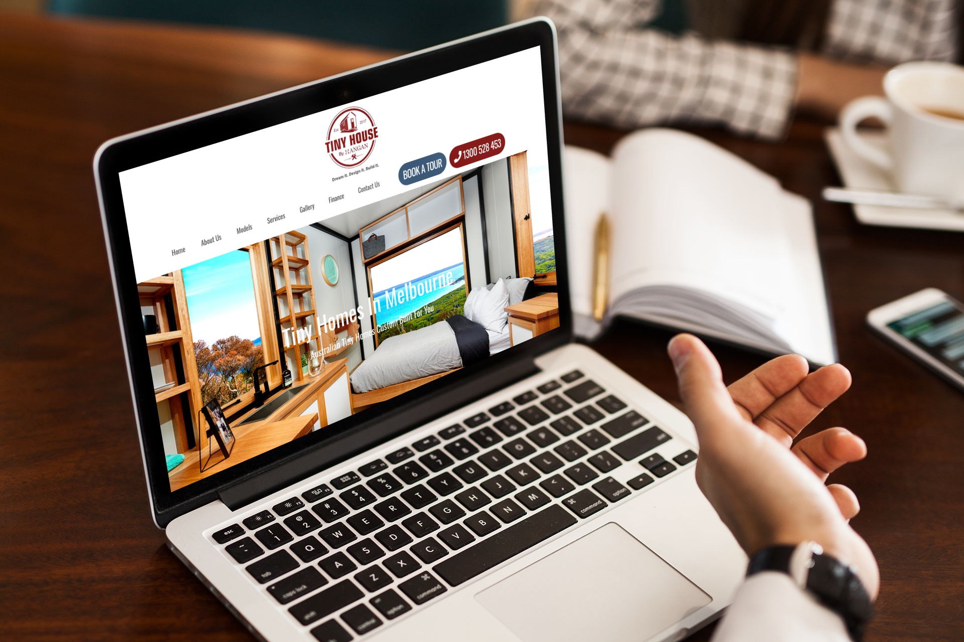 Laptop displaying a website with a cabin interior photo; a person's hand with a watch on the laptop keyboard.