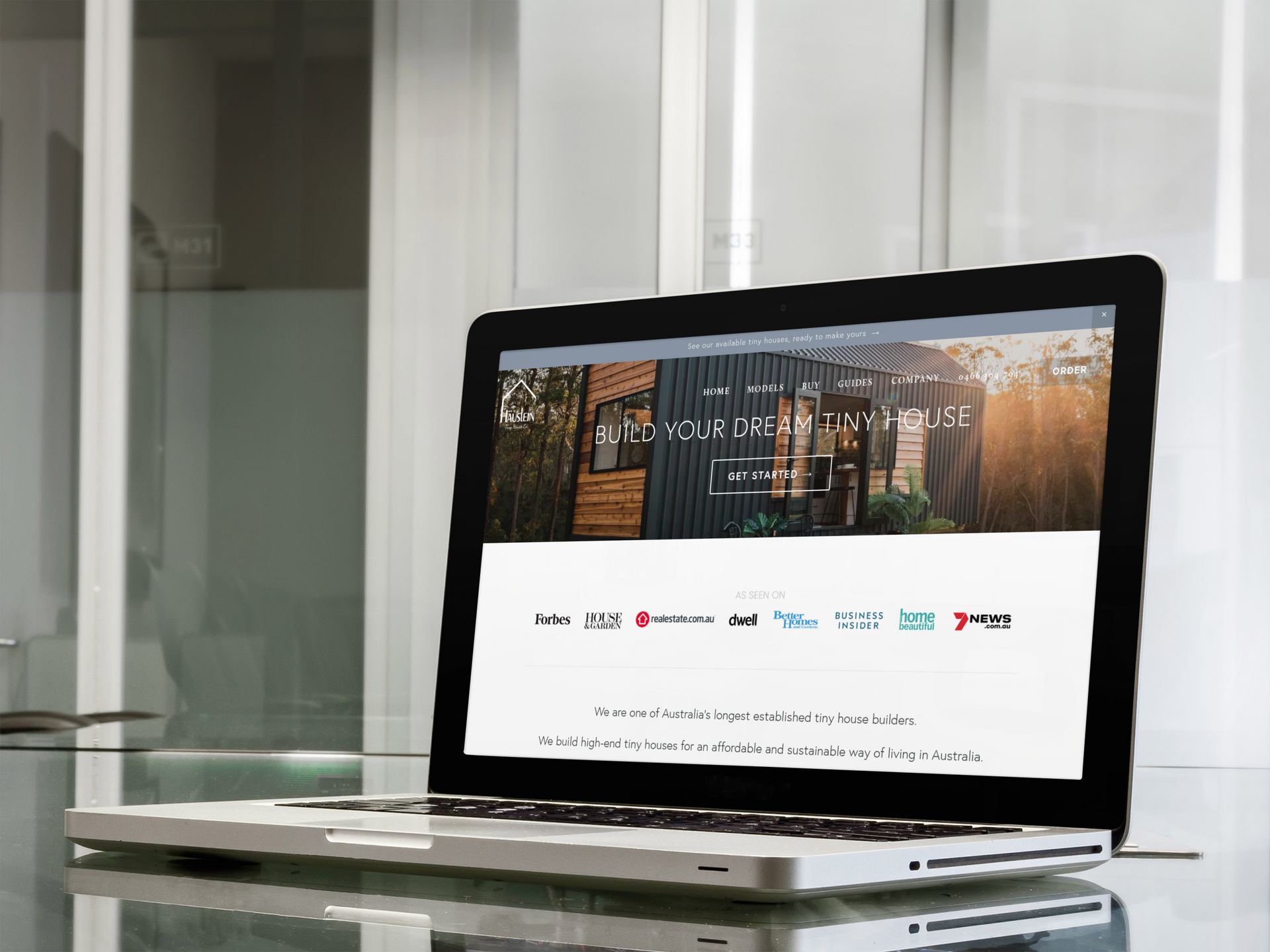 Laptop displaying a website, on a glass table in an office setting.