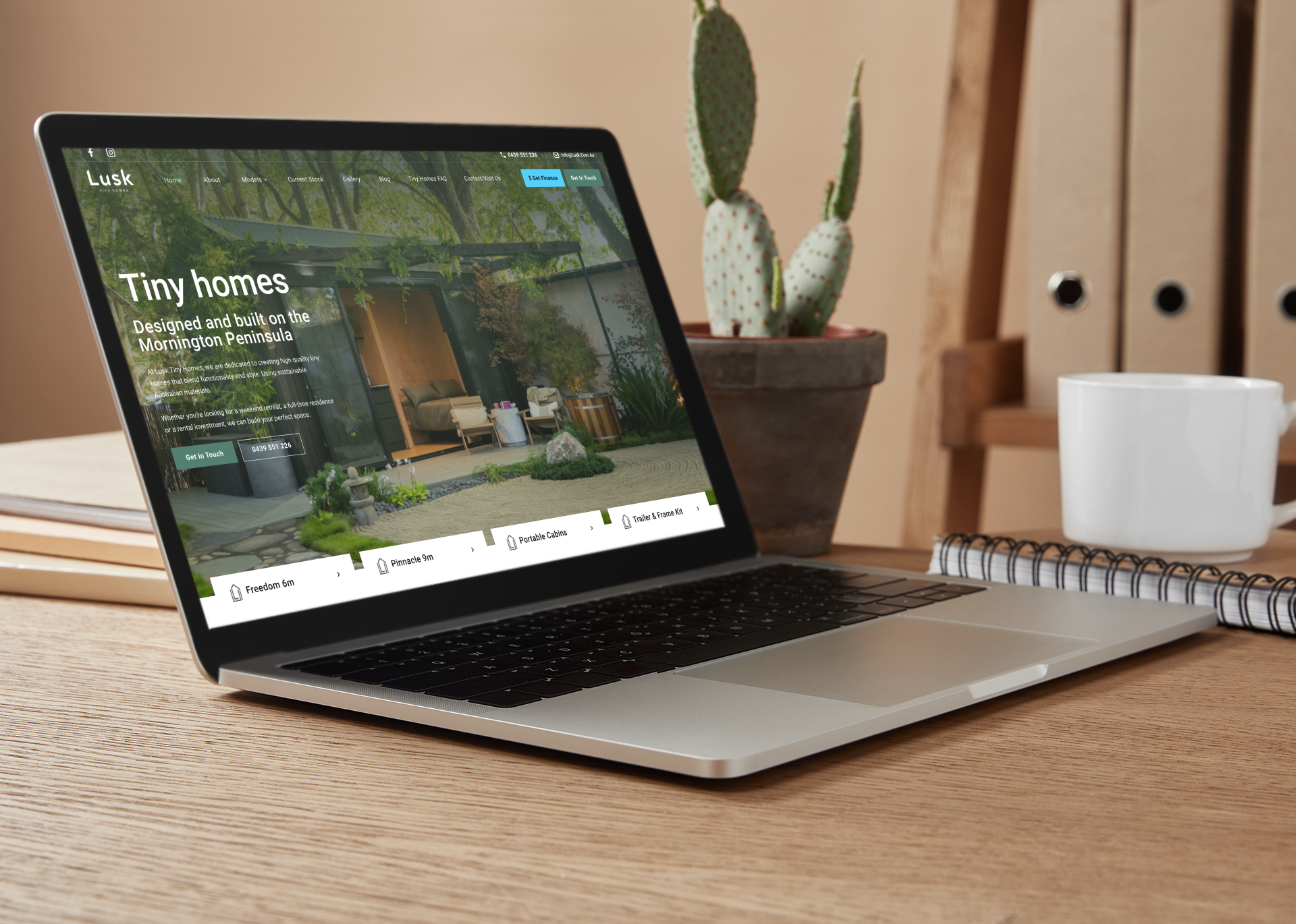 Laptop displaying a tiny home website, with a cactus and coffee cup in the background.