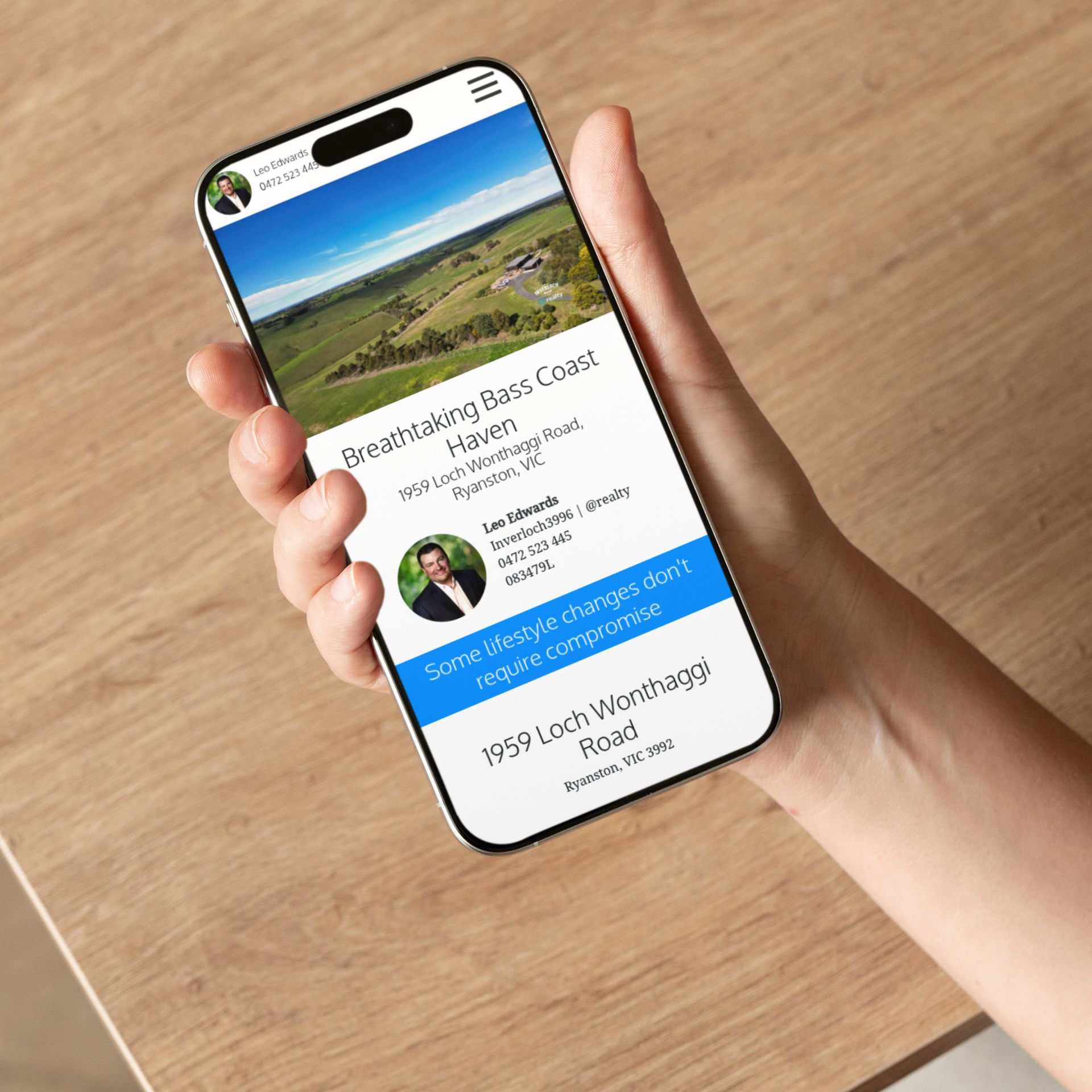Person holding a smartphone showcasing a real estate listing: aerial view of a property, contact info, and tagline.