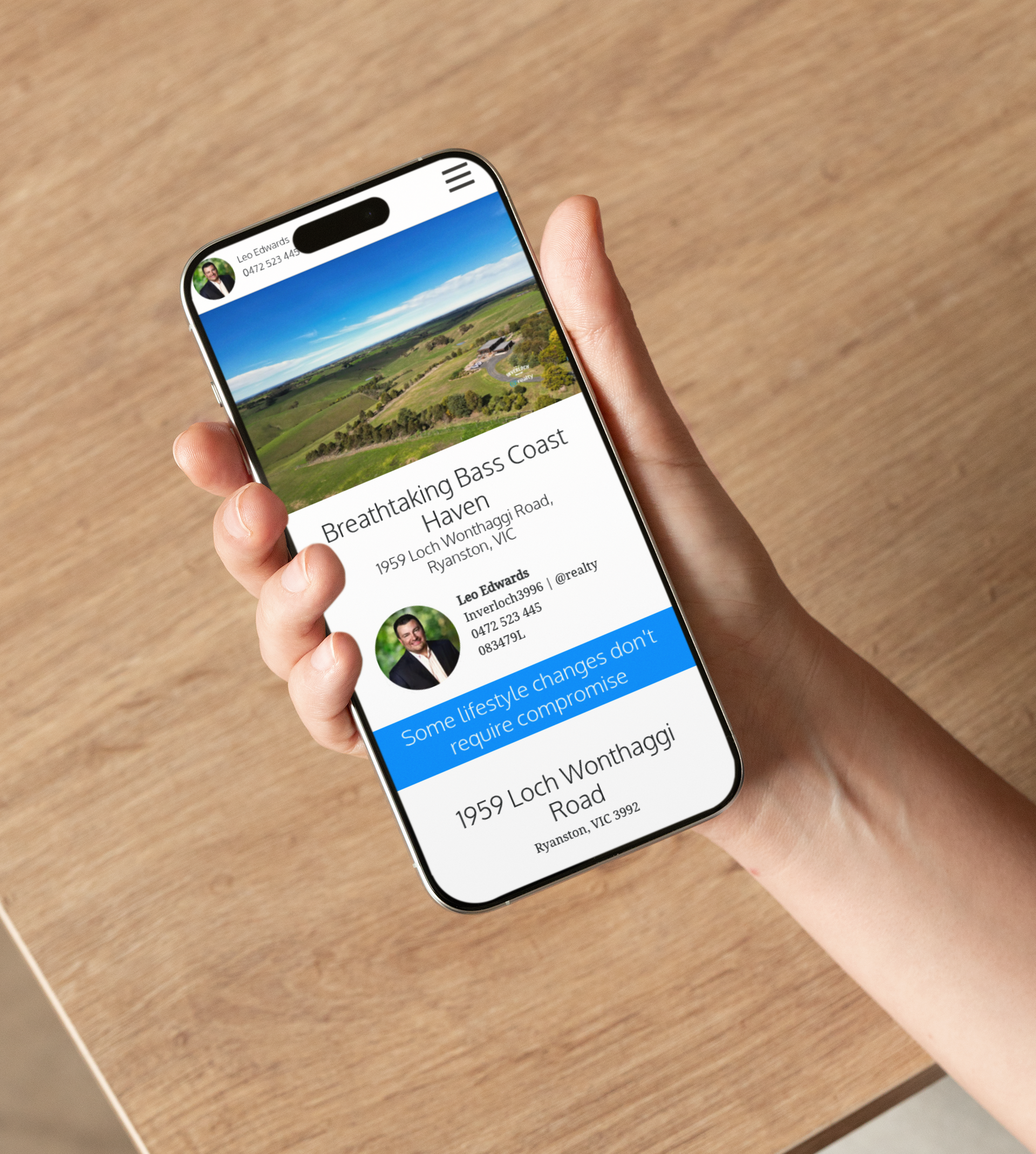 Hand holding a smartphone, displaying a webpage about a property, blue sky, green fields, and a person's headshot.