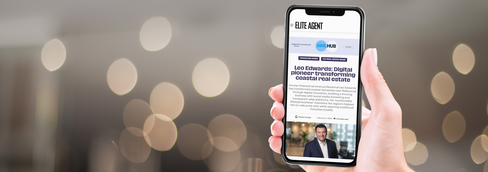 Person holding a smartphone displaying an article about a man in a blazer. Blurred background with bokeh.