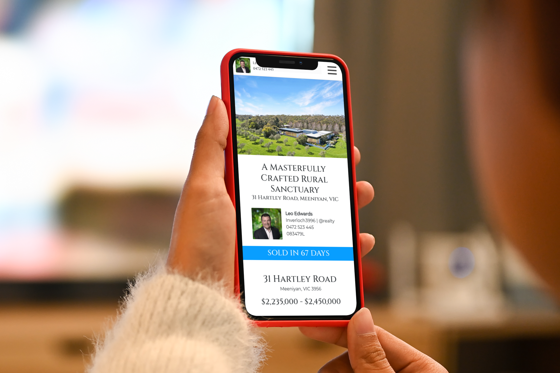 Person holding red phone displaying a real estate listing.
