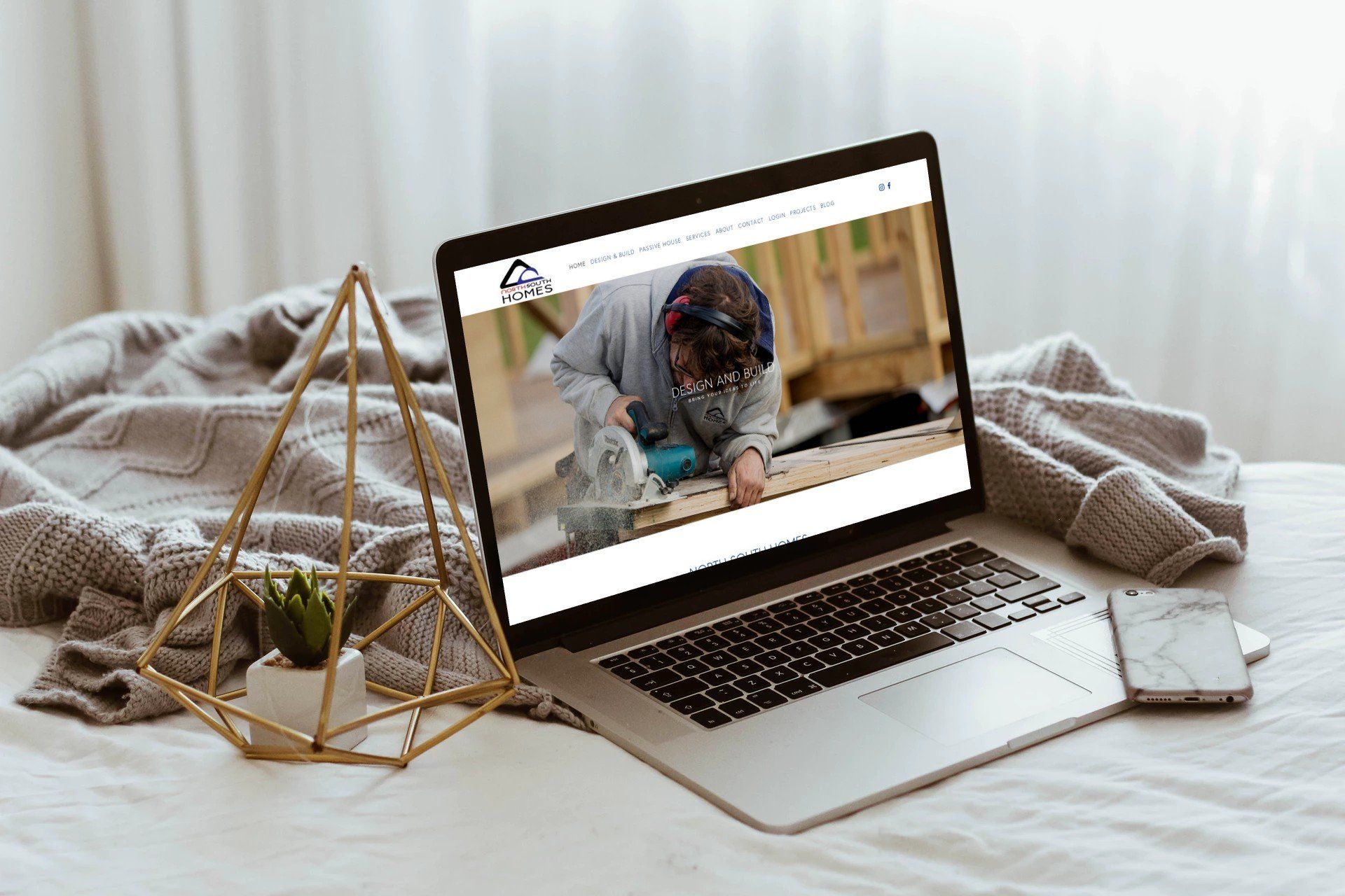 A laptop computer is sitting on a bed next to a phone and a plant.