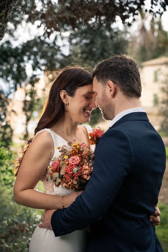 Wedding couple embracing, smiling, outdoors, woman holding bouquet.