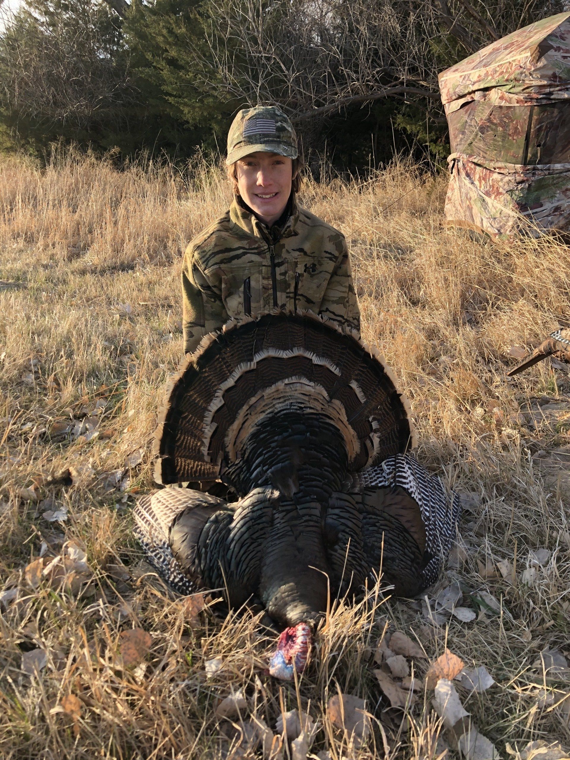 A man is kneeling down next to a large turkey in a field.