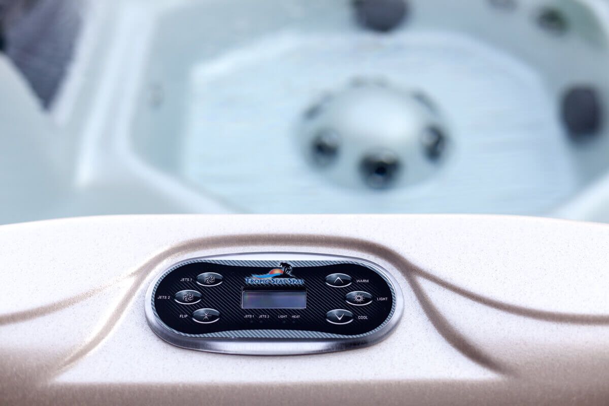 Close-up of a hot tub control panel with buttons and a digital display. The tub is filled with water.