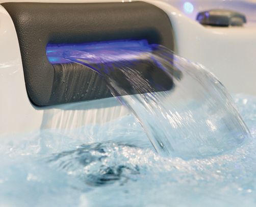 Close-up of a spa water feature with a blue light illuminating cascading water into a bubbly spa pool.