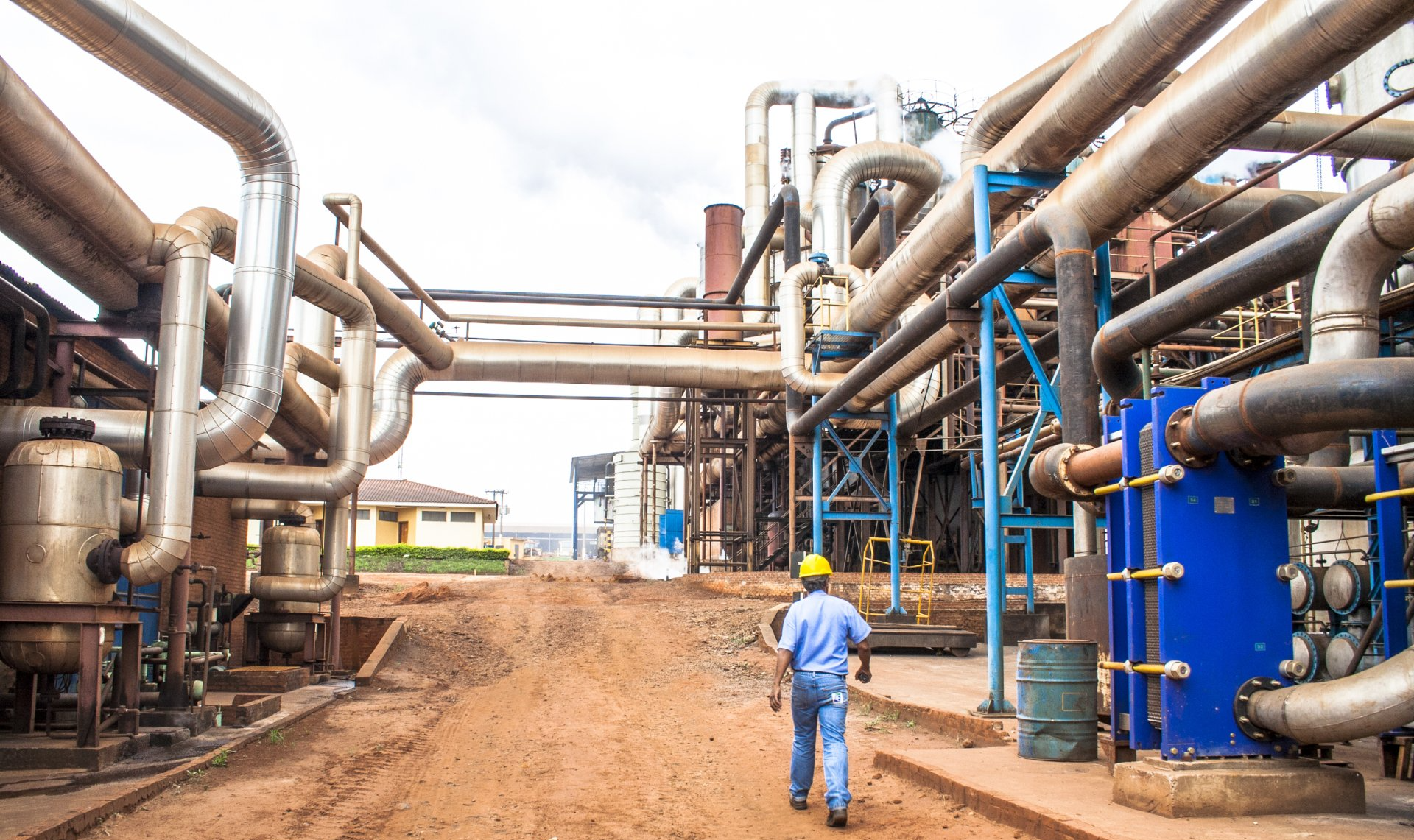 A man is walking through a factory filled with pipes.