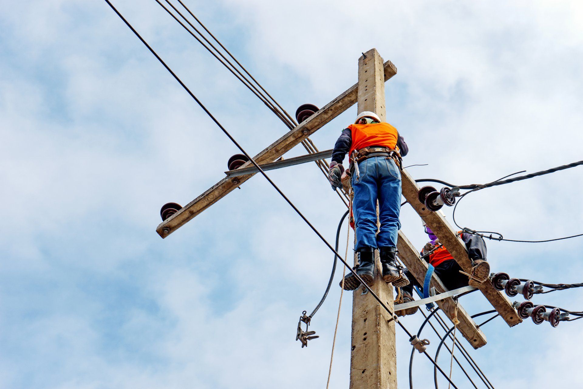 Two men are standing on top of a wooden power pole.