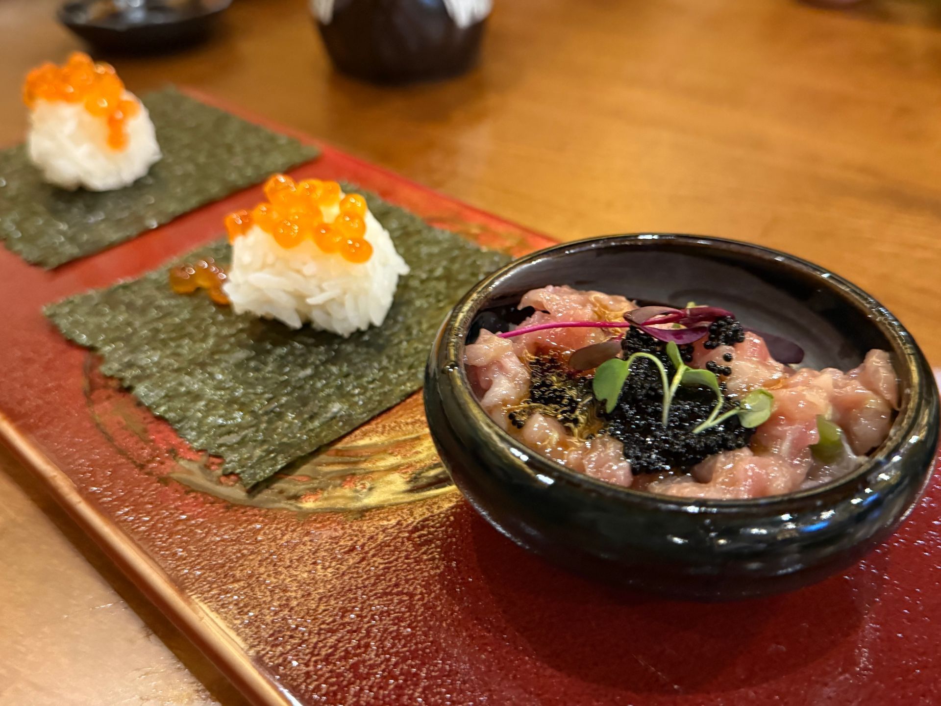 Sushi and seaweed-wrapped rice on a red tray with a small bowl of dipping sauce