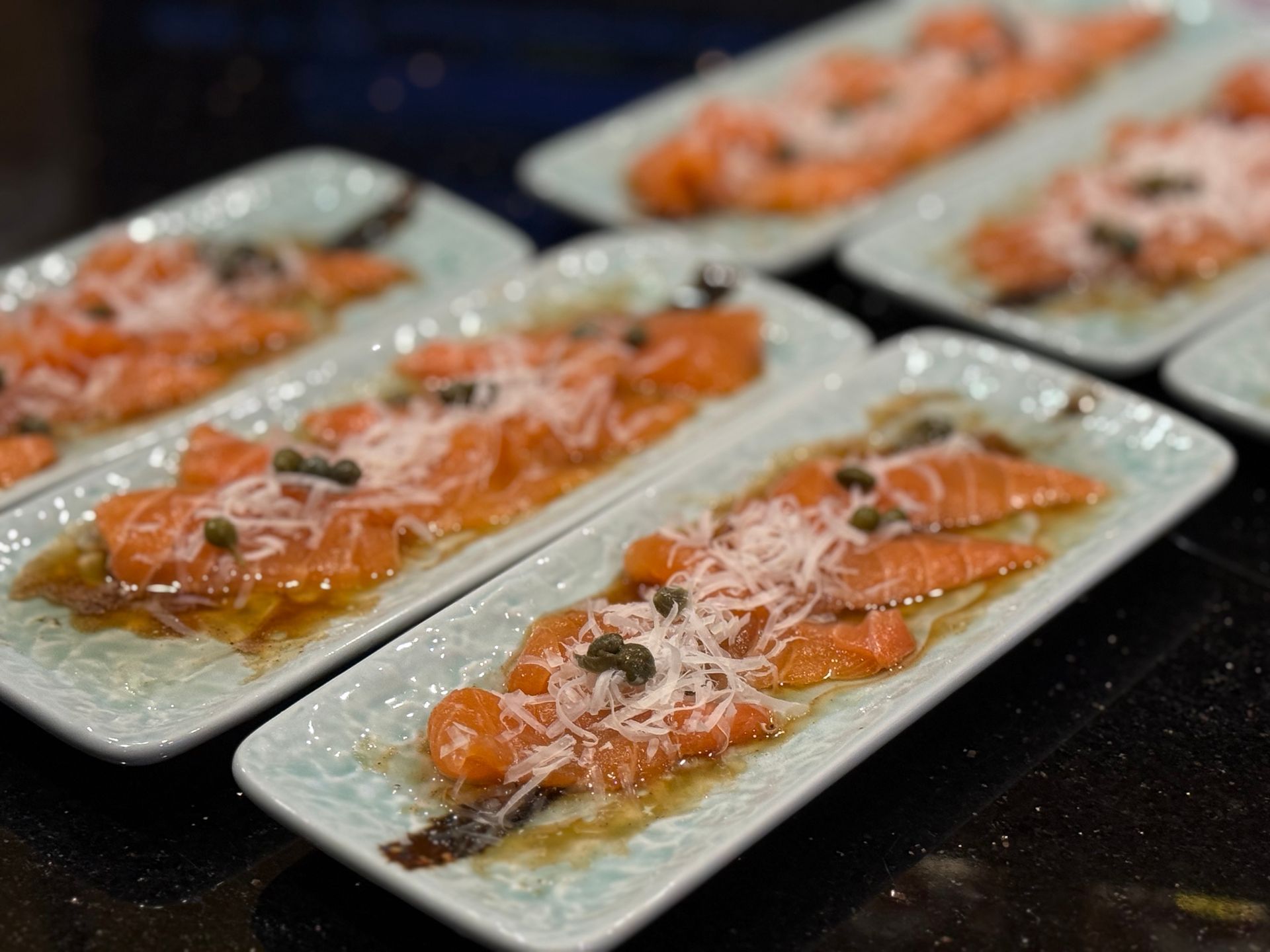 Plated salmon slices topped with herbs and sauce on rectangular white dishes, arranged on a table